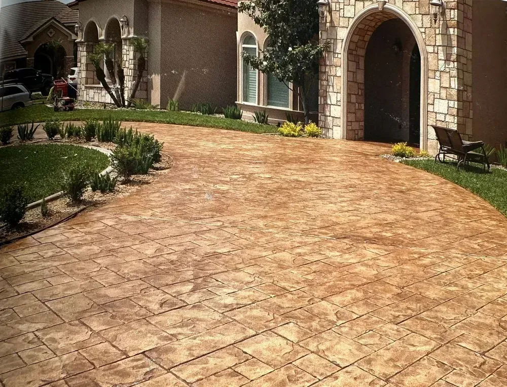 Stone-patterned driveway leading to a house with an arched stone entry and landscaped greenery