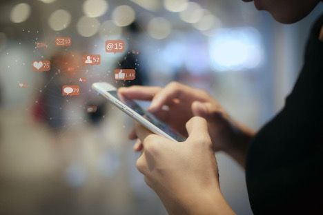 Woman using smartphone, surrounded by social media notification icons, blurred background.