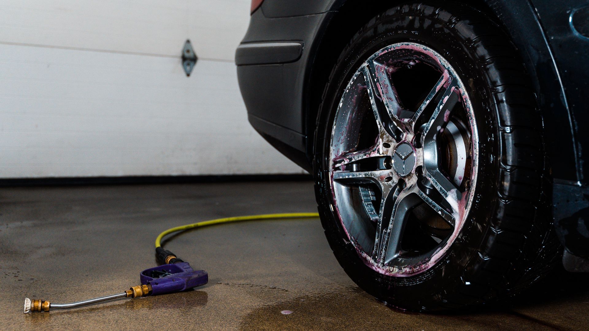 A car is being washed in a garage with a hose attached to it.