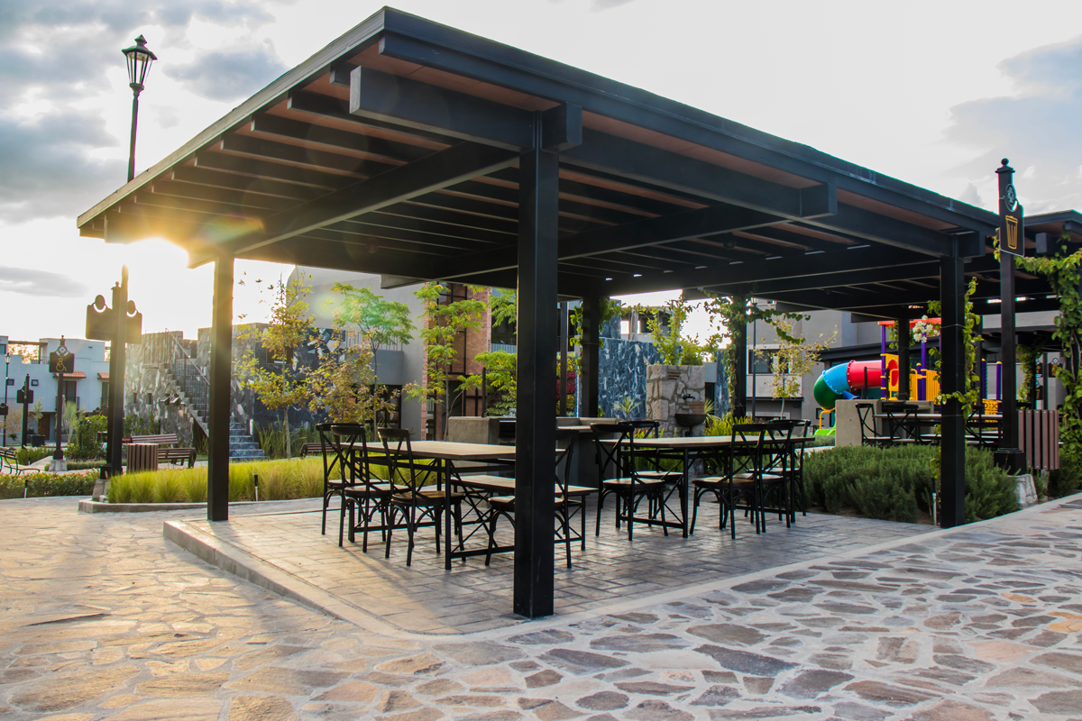 Una pérgola con mesas y sillas debajo en un parque.