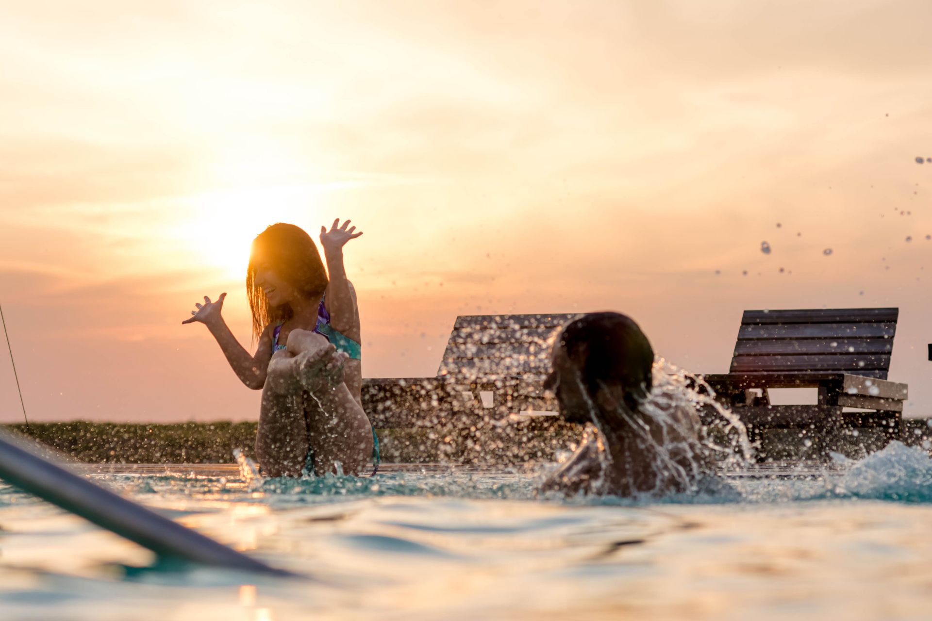 Un hombre y una niña están jugando en una piscina al atardecer.