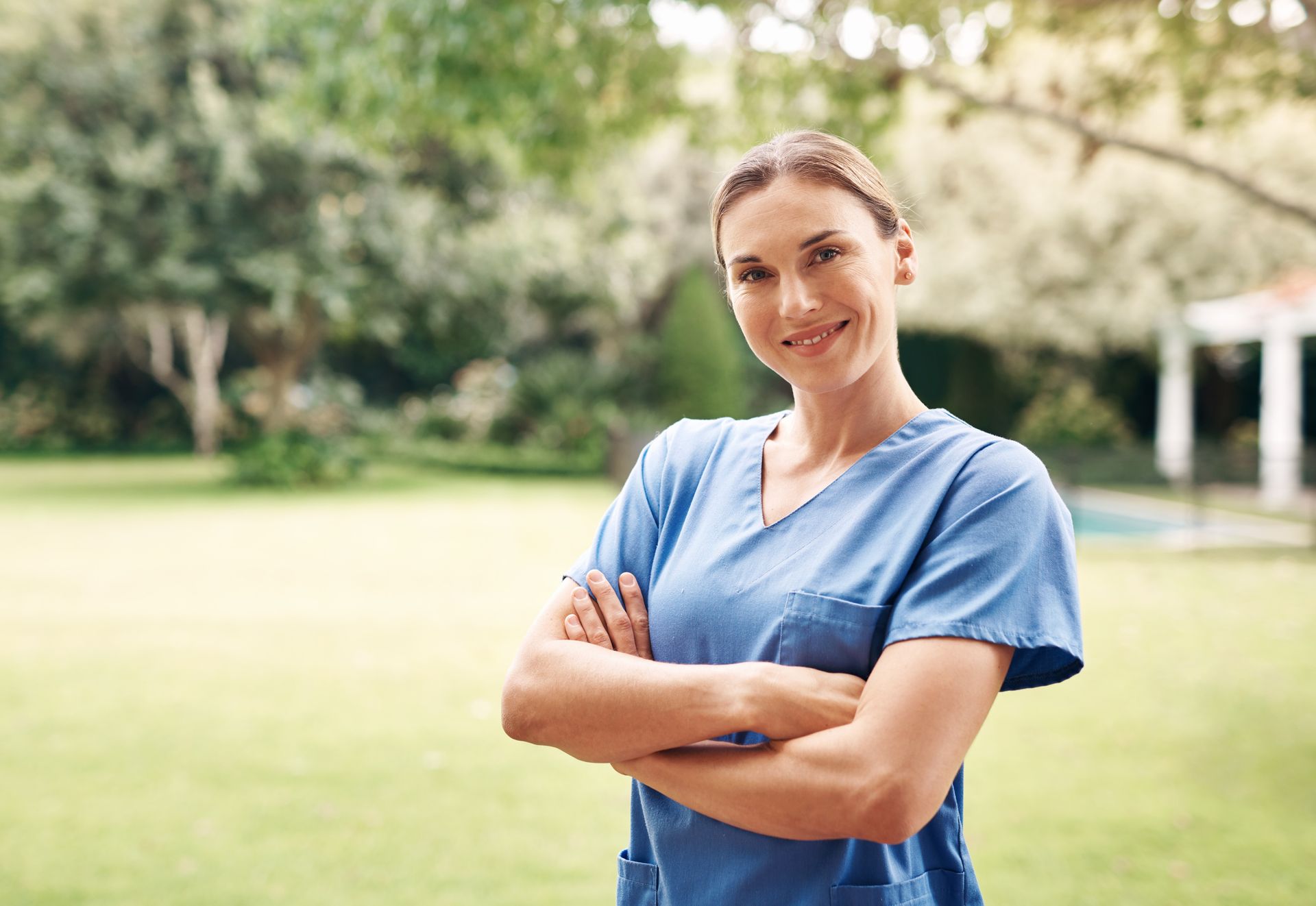 Un'infermiera è in piedi in un parco con le braccia incrociate e sorridente.