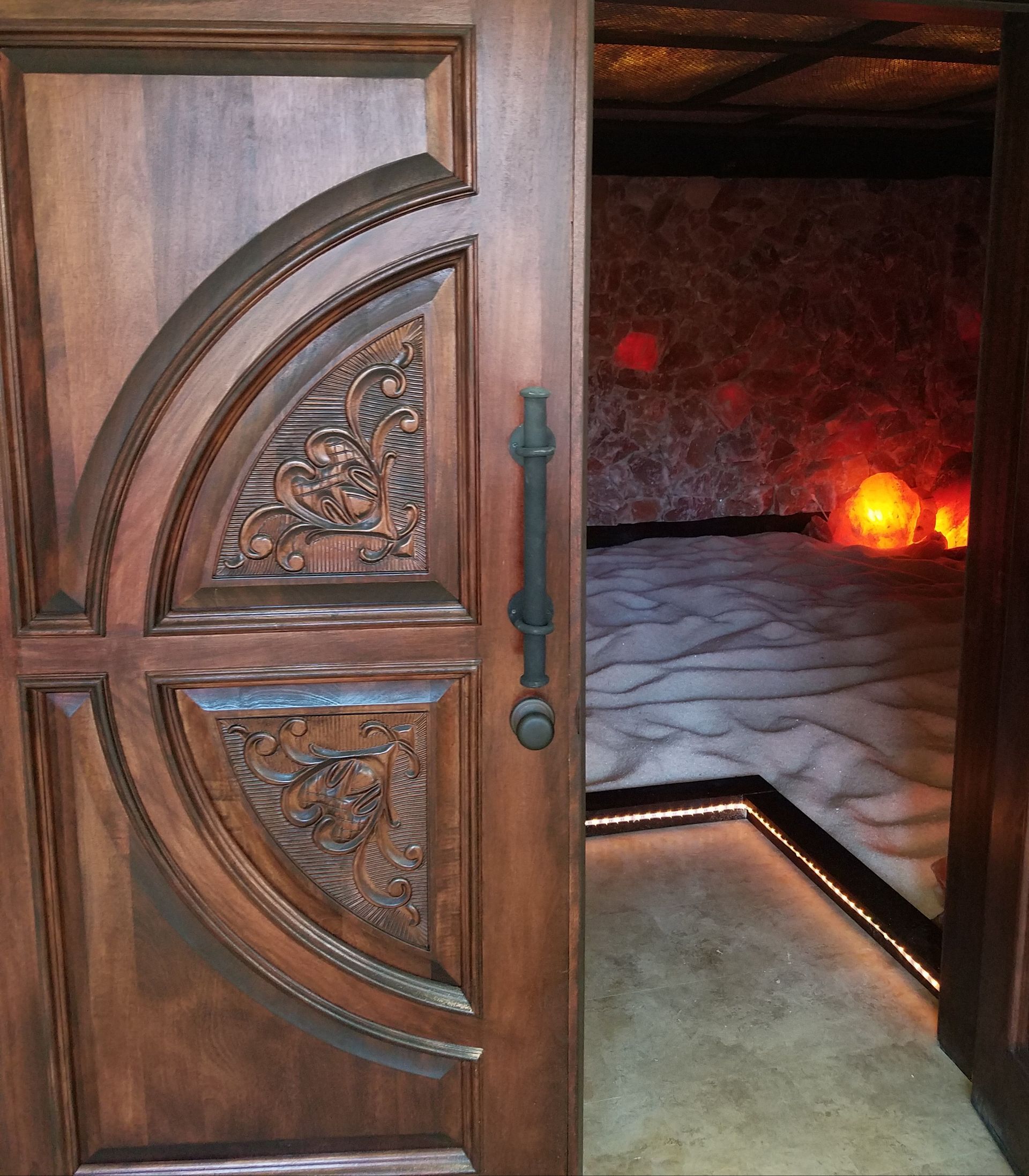 Wooden door with ornate carving, open to a dimly lit salt room.