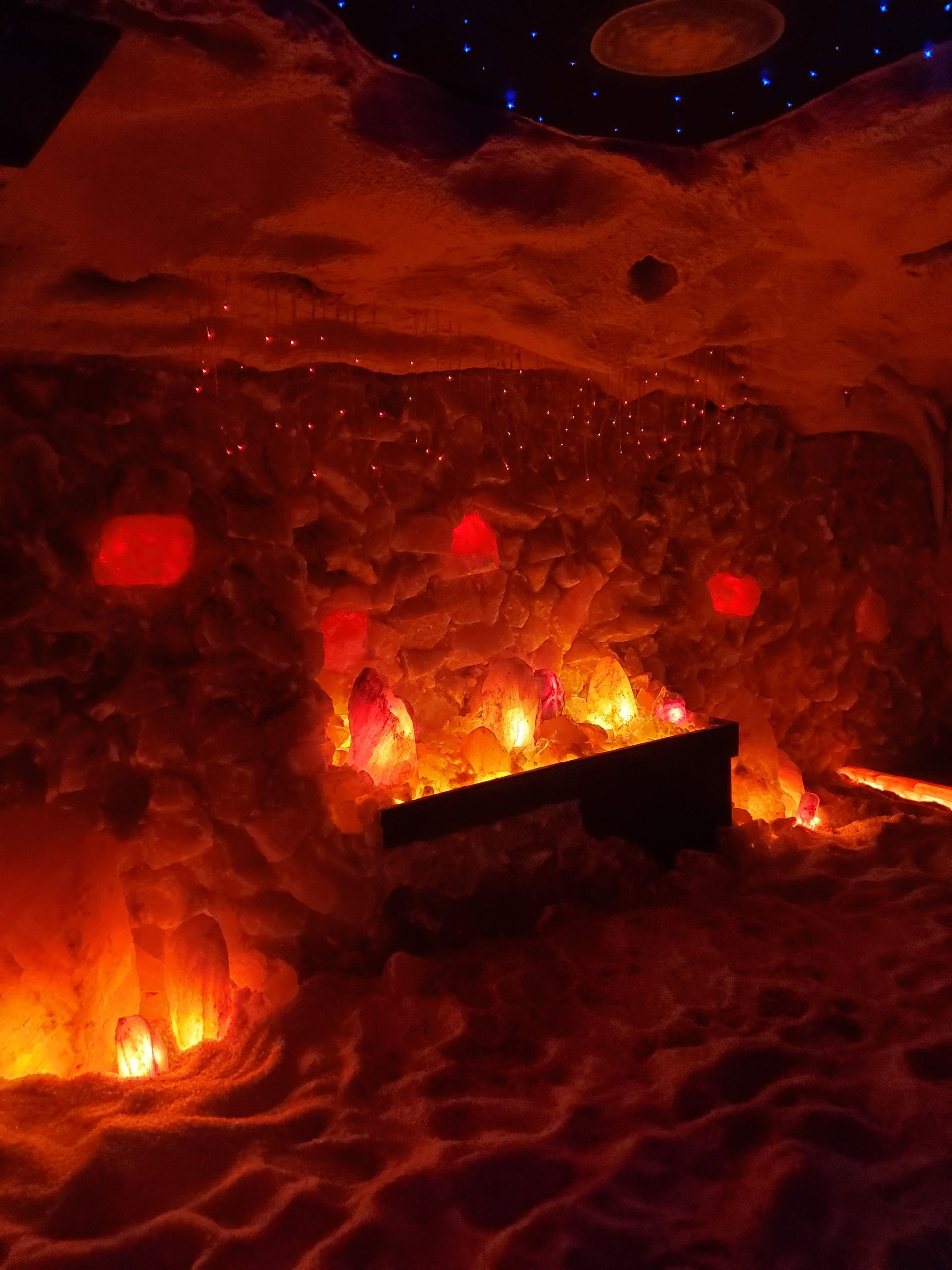 A dimly lit salt cave with orange and red light. Crystals and a bench are visible.