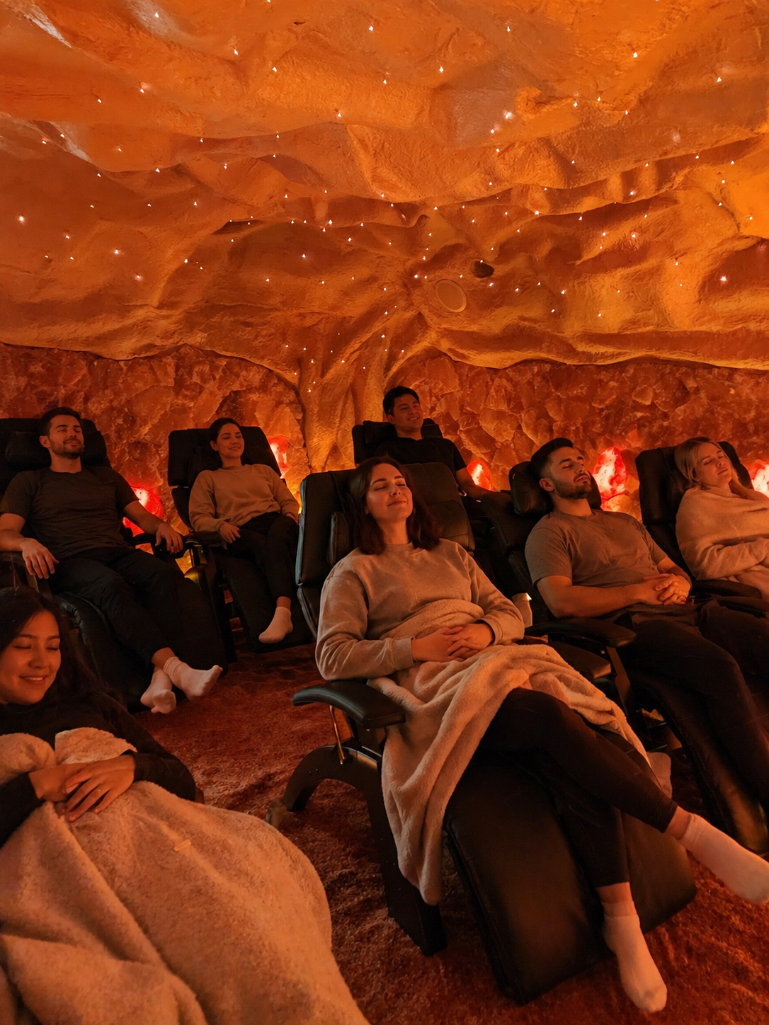 People reclining in chairs inside an orange-lit, cave-like room, watching a presentation