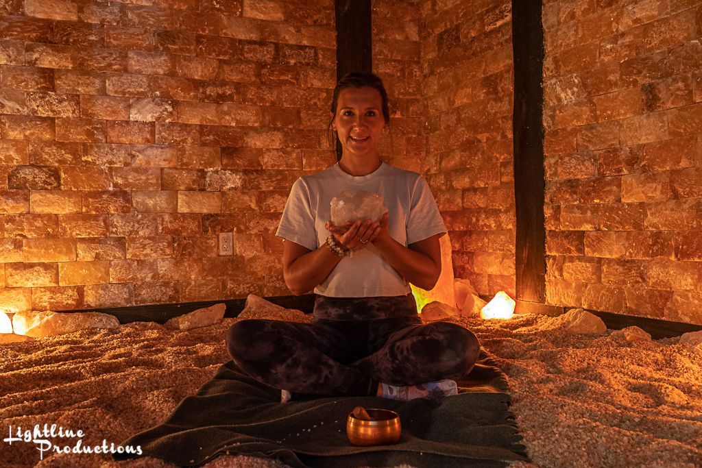 A woman is sitting in a lotus position in a room with a brick wall.