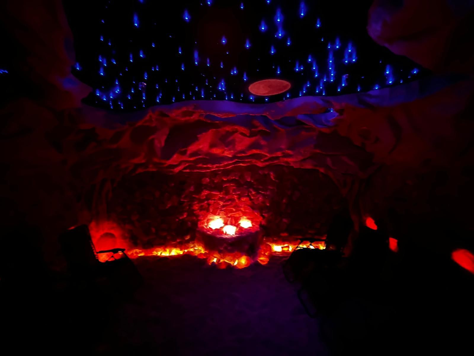 There is a fire in the middle of the room with a starry sky in the background.