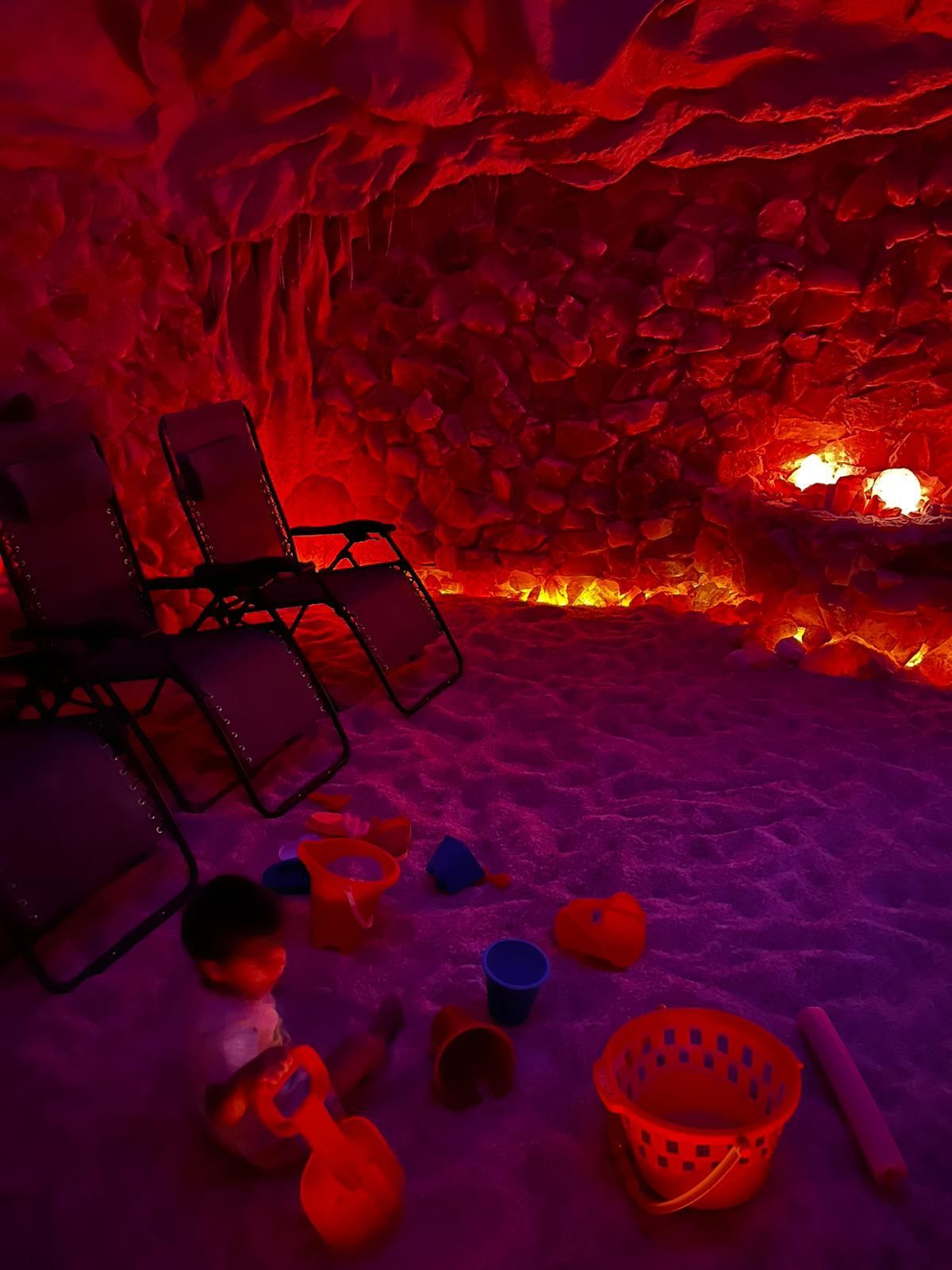Salt cave interior with red and purple lighting, lounge chairs, and children's beach toys.