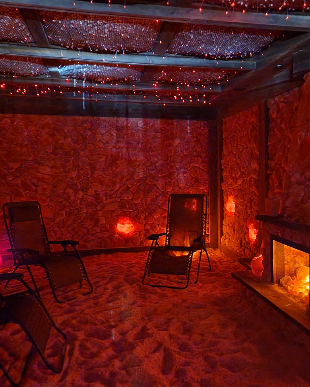Salt room interior with red-lit walls, reclining chairs, and a fireplace, creating a relaxing atmosphere.