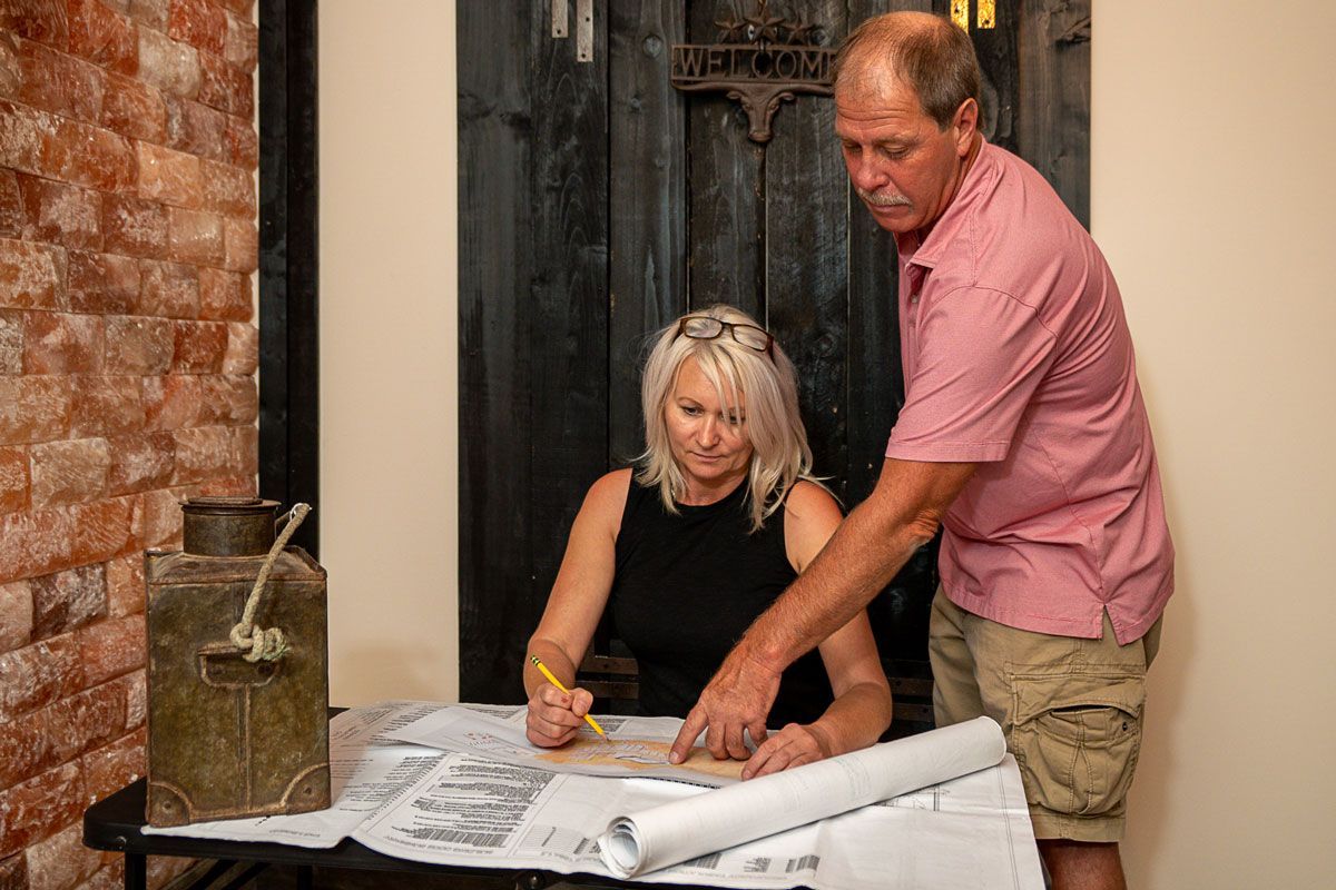 A man and a woman are sitting at a table looking at blueprints.