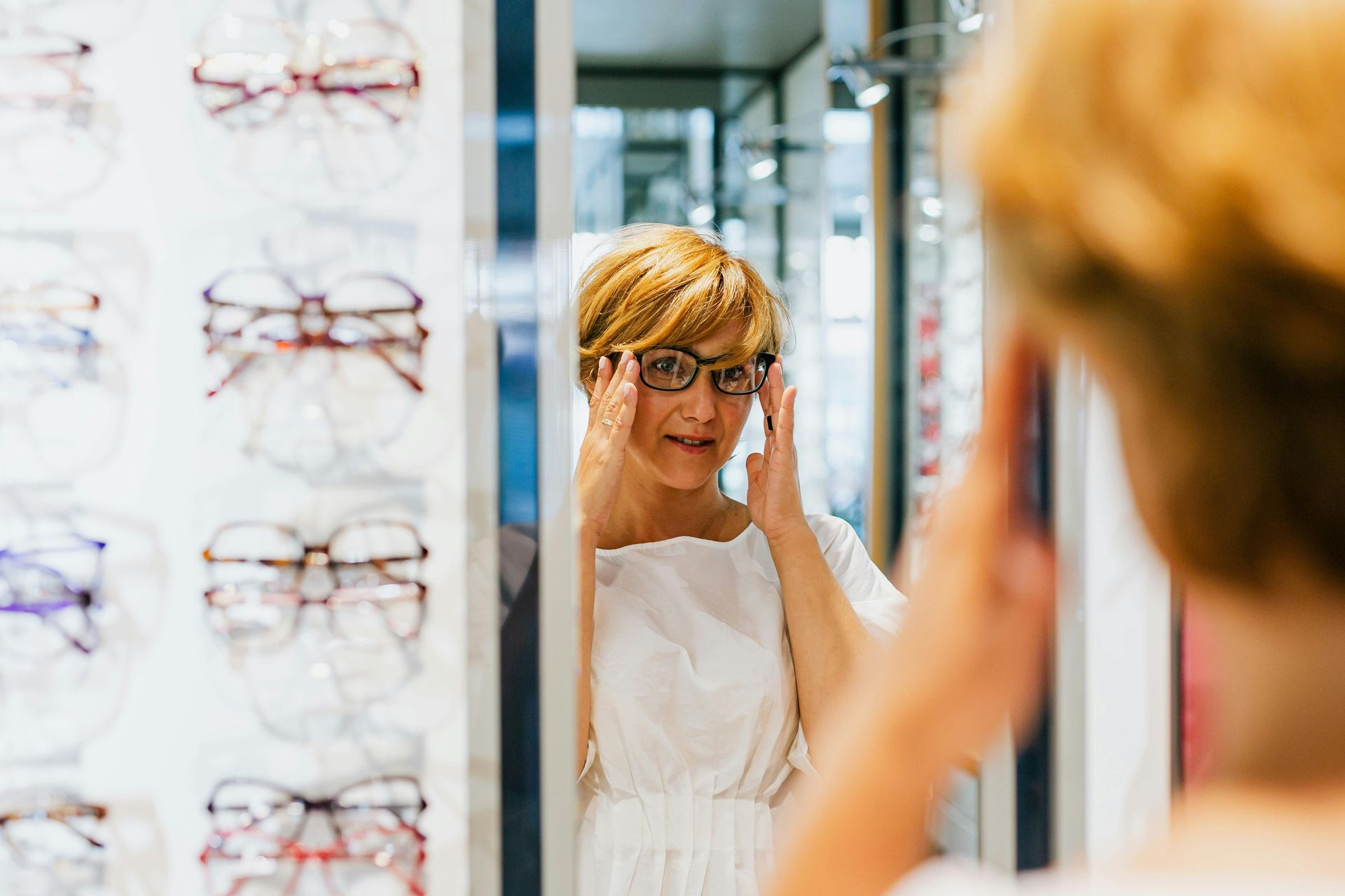 Une femme essaie des lunettes devant un miroir.