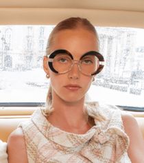 Une femme portant des lunettes rondes est assise dans une voiture.
