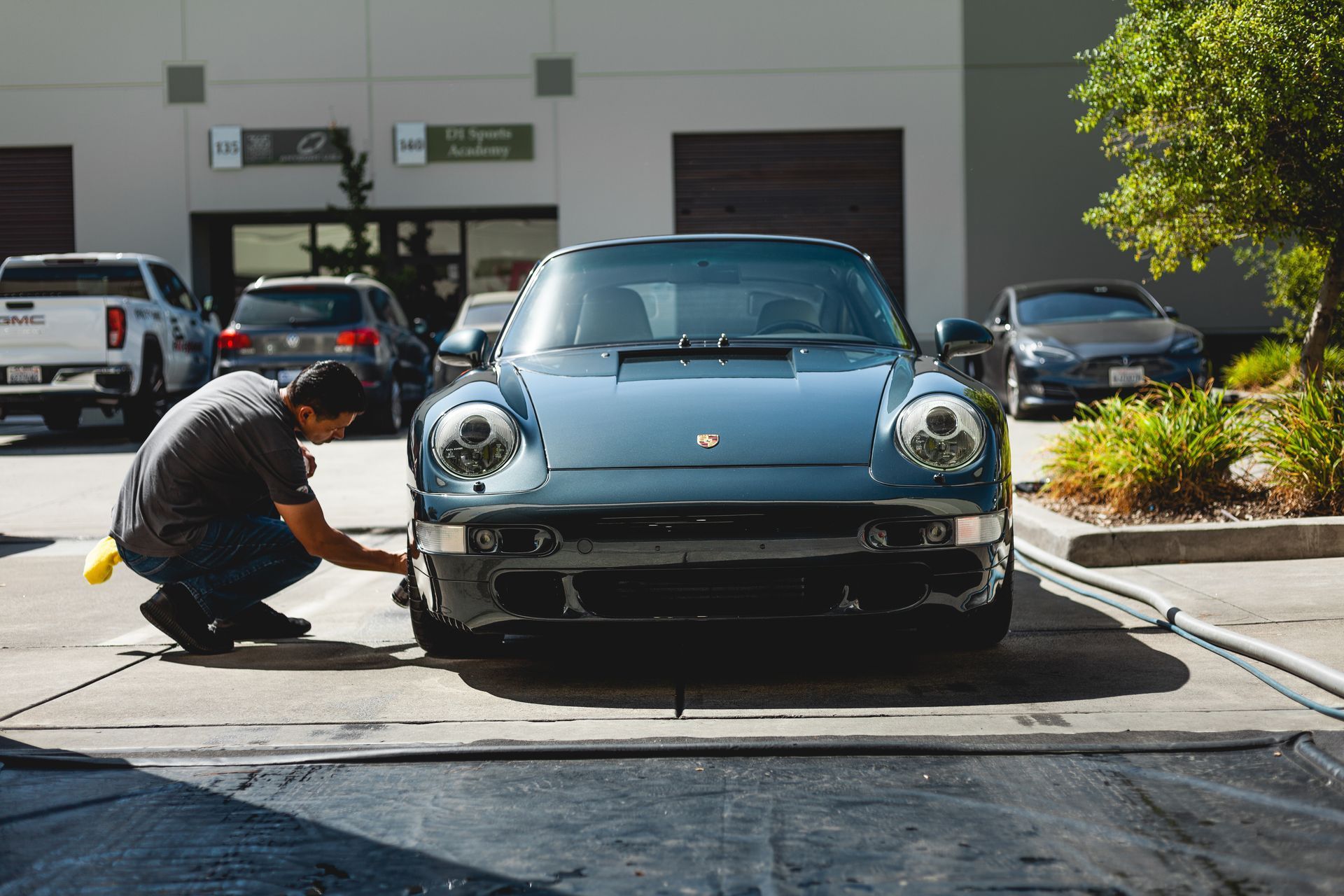 Man detailing a dark blue Porsche sports car in front of a building.