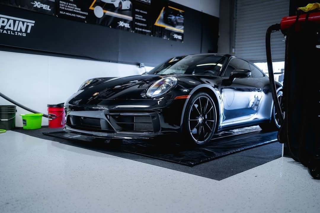 Black Porsche sports car inside a garage, next to cleaning supplies.