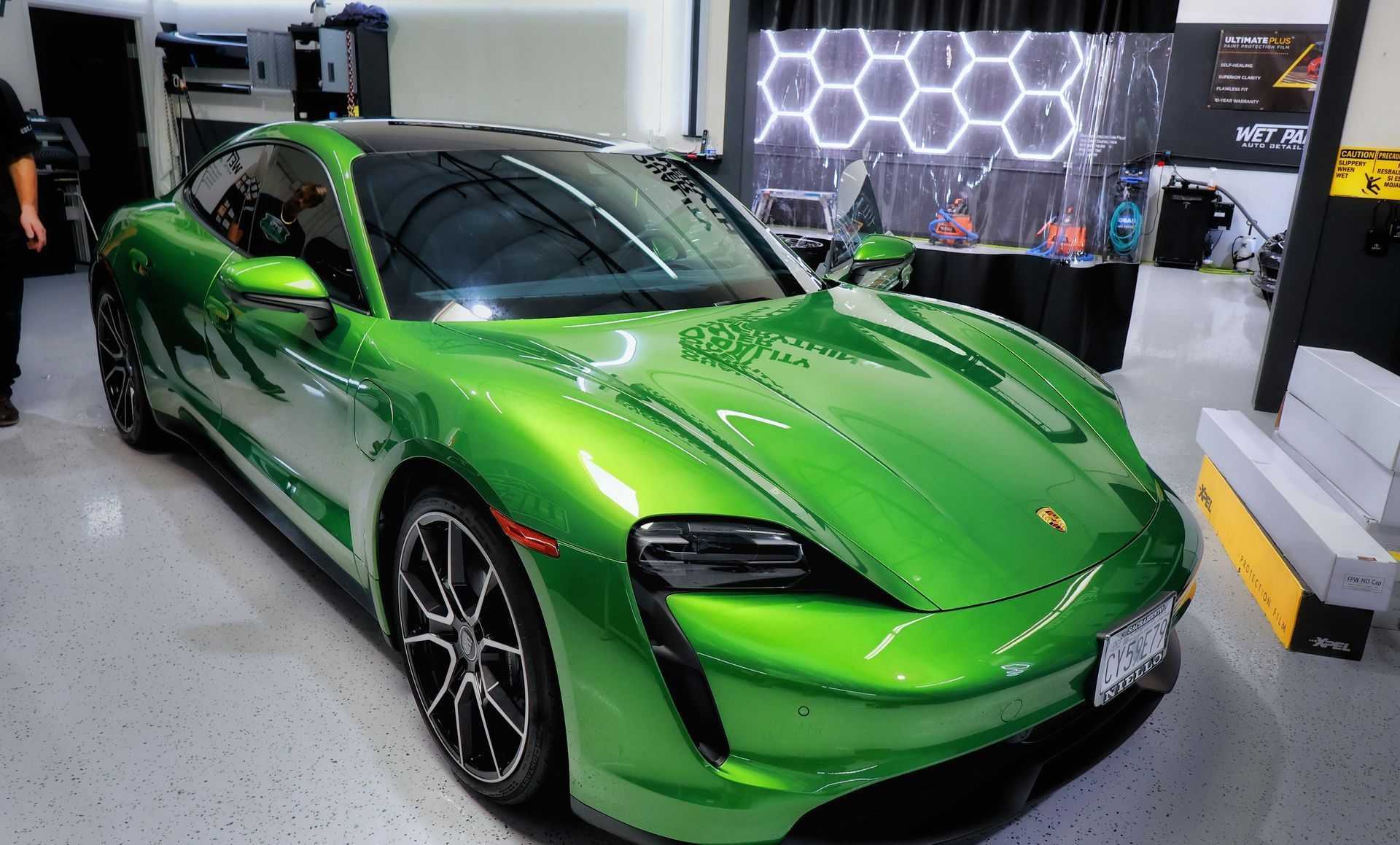 Green Porsche Taycan electric car in a garage with black wheels.