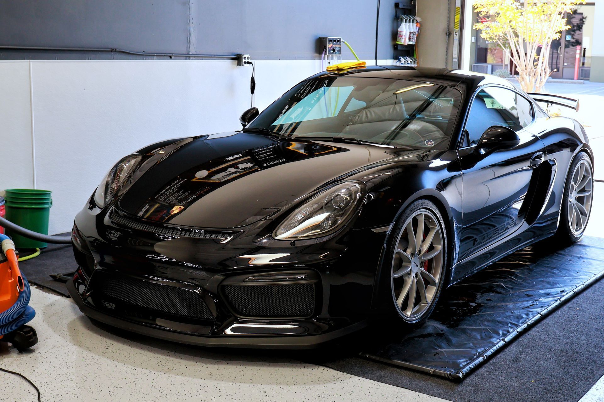 Black Porsche sports car in a garage, shiny and parked on a mat.
