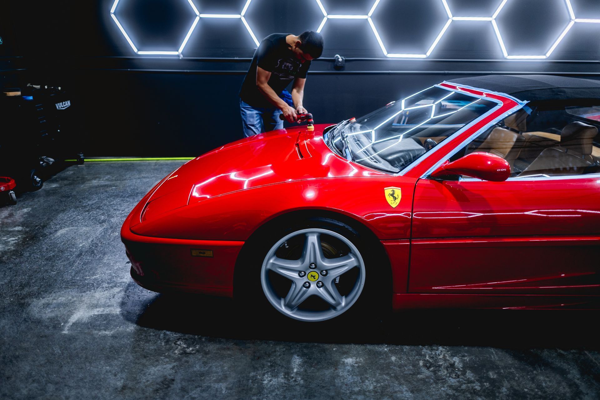 A man is polishing a red ferrari convertible in a garage.