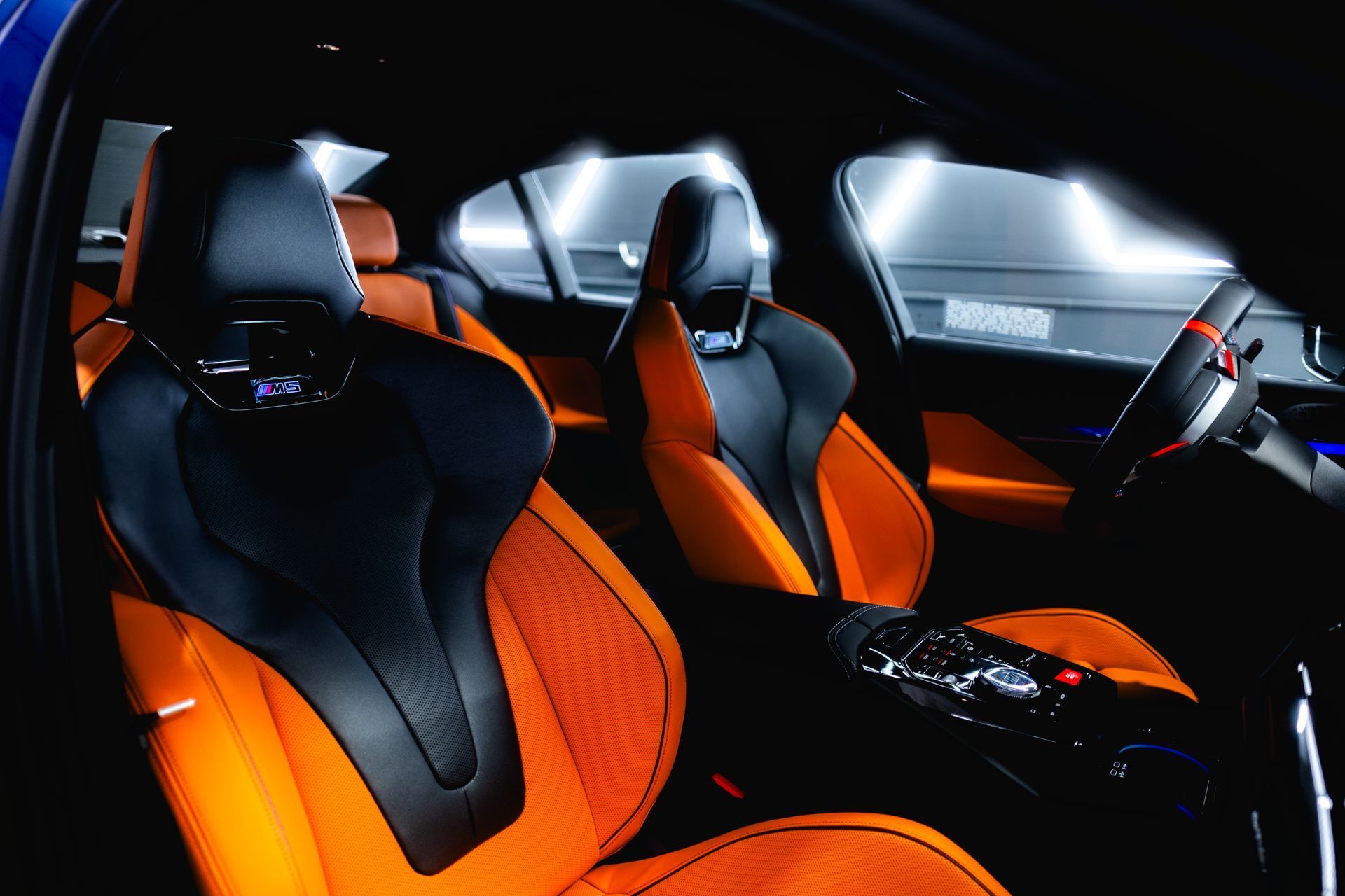 Interior of a car with orange and black sport seats, illuminated by overhead lights.