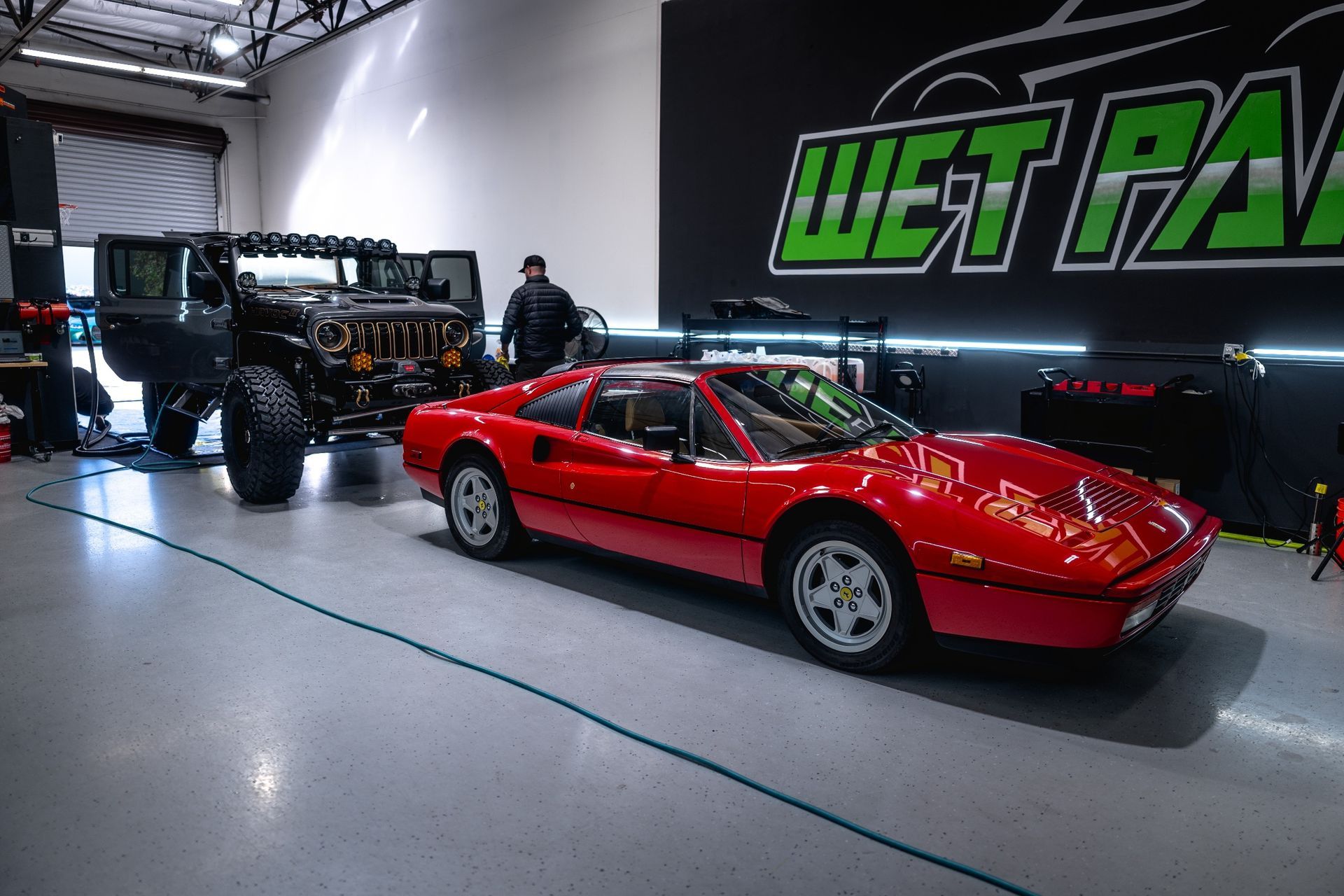 A red sports car is parked in a garage next to a jeep.