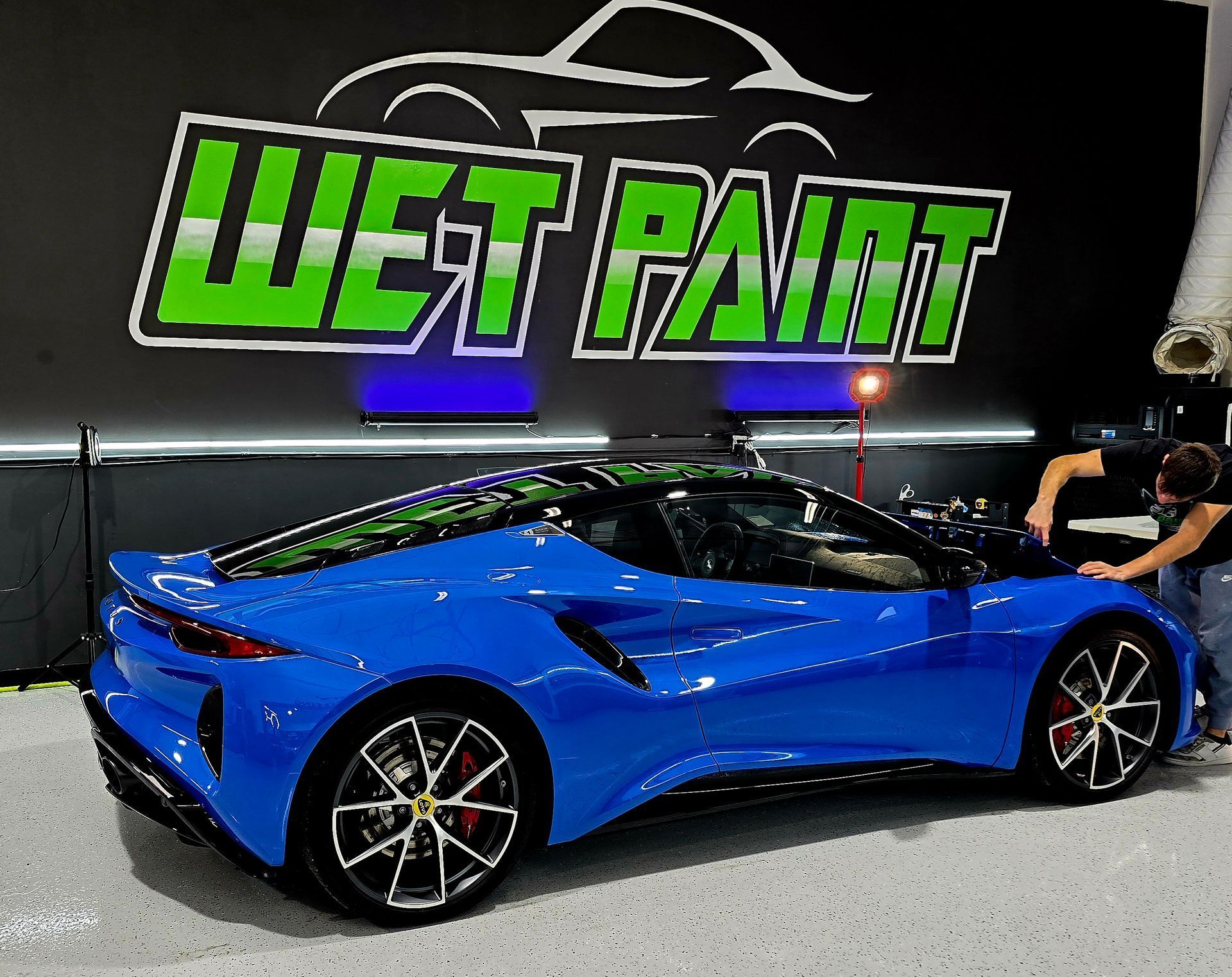 A blue sports car is parked in front of a wet paint sign