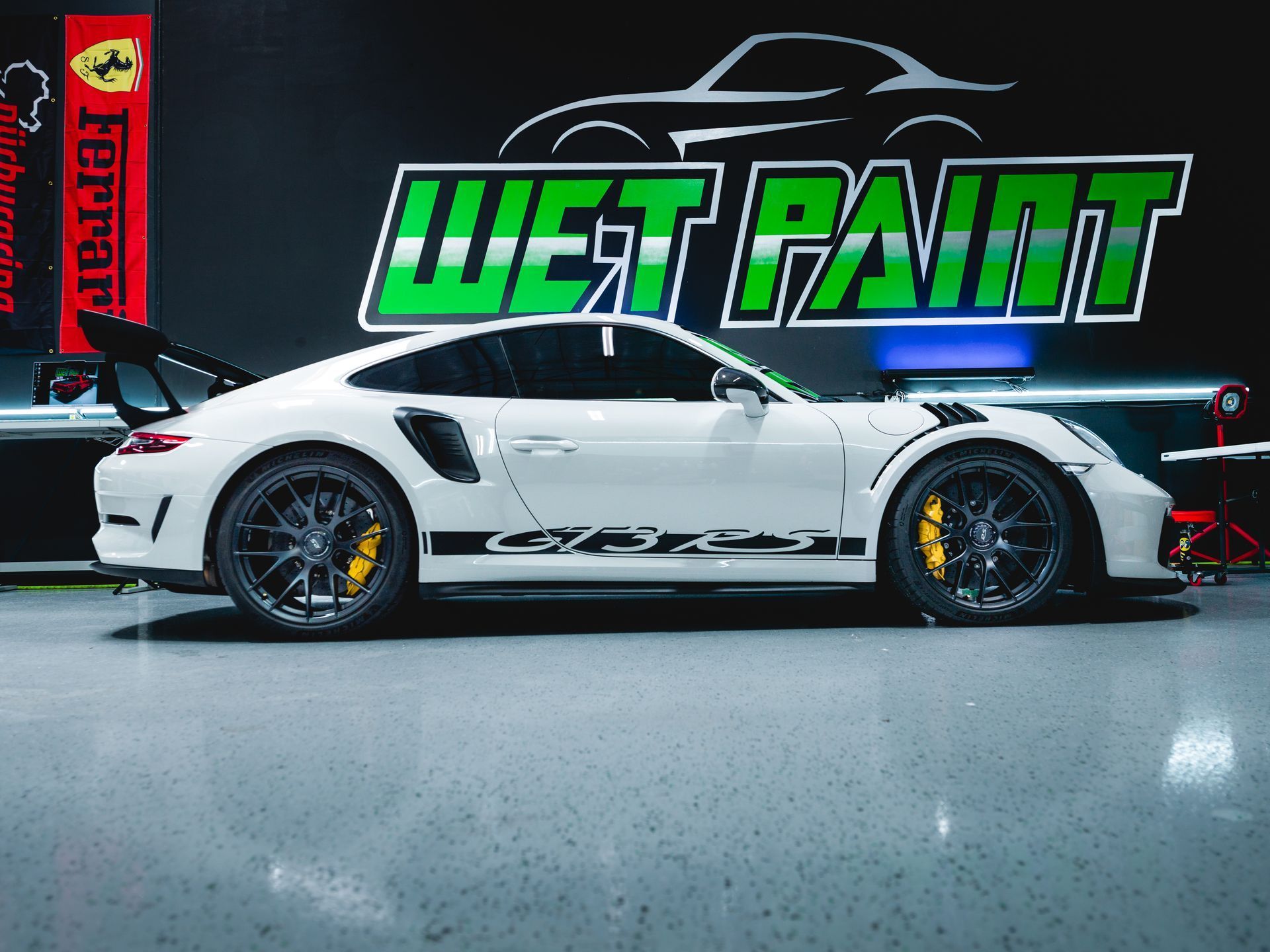 A white Porsche 911 GT3 RS with yellow brake calipers parked in a professional garage with 