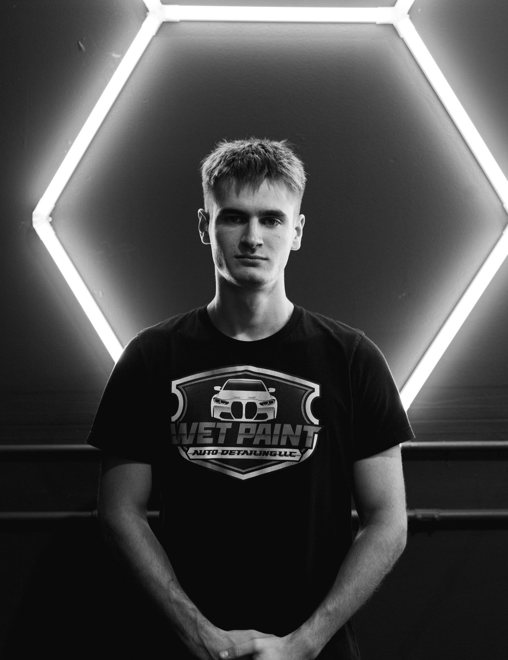 A man in a black t-shirt is standing in front of a hexagon of lights.