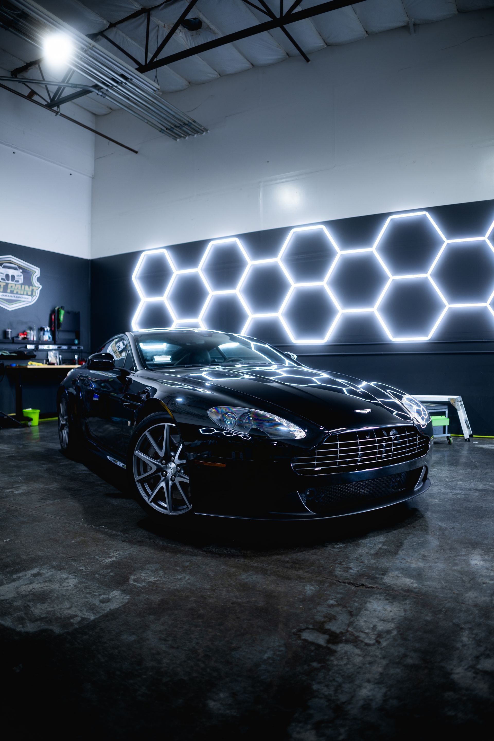 A black sports car is parked in a garage with honeycomb lights on the wall.