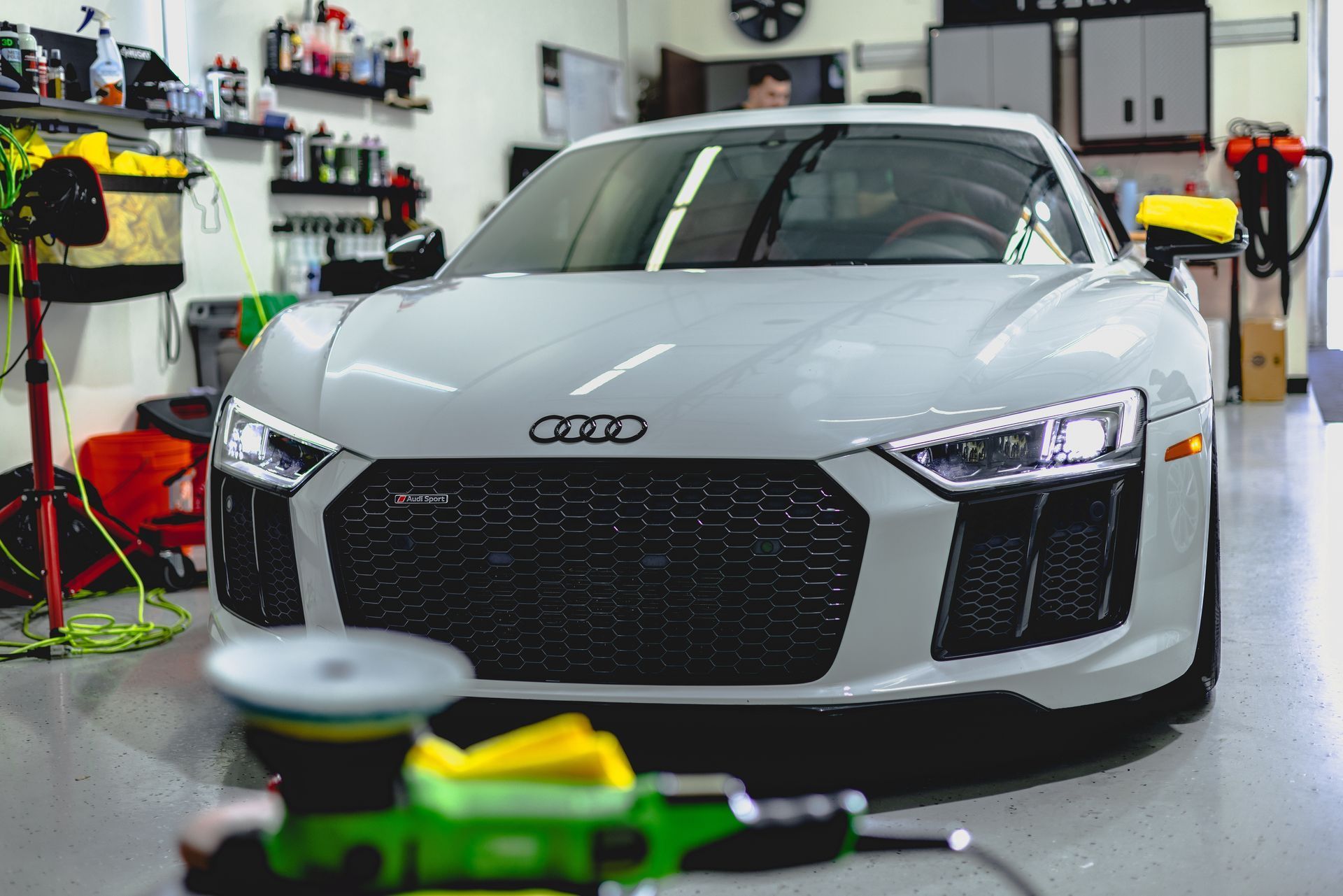 A white audi r8 is parked in a garage next to a green machine.
