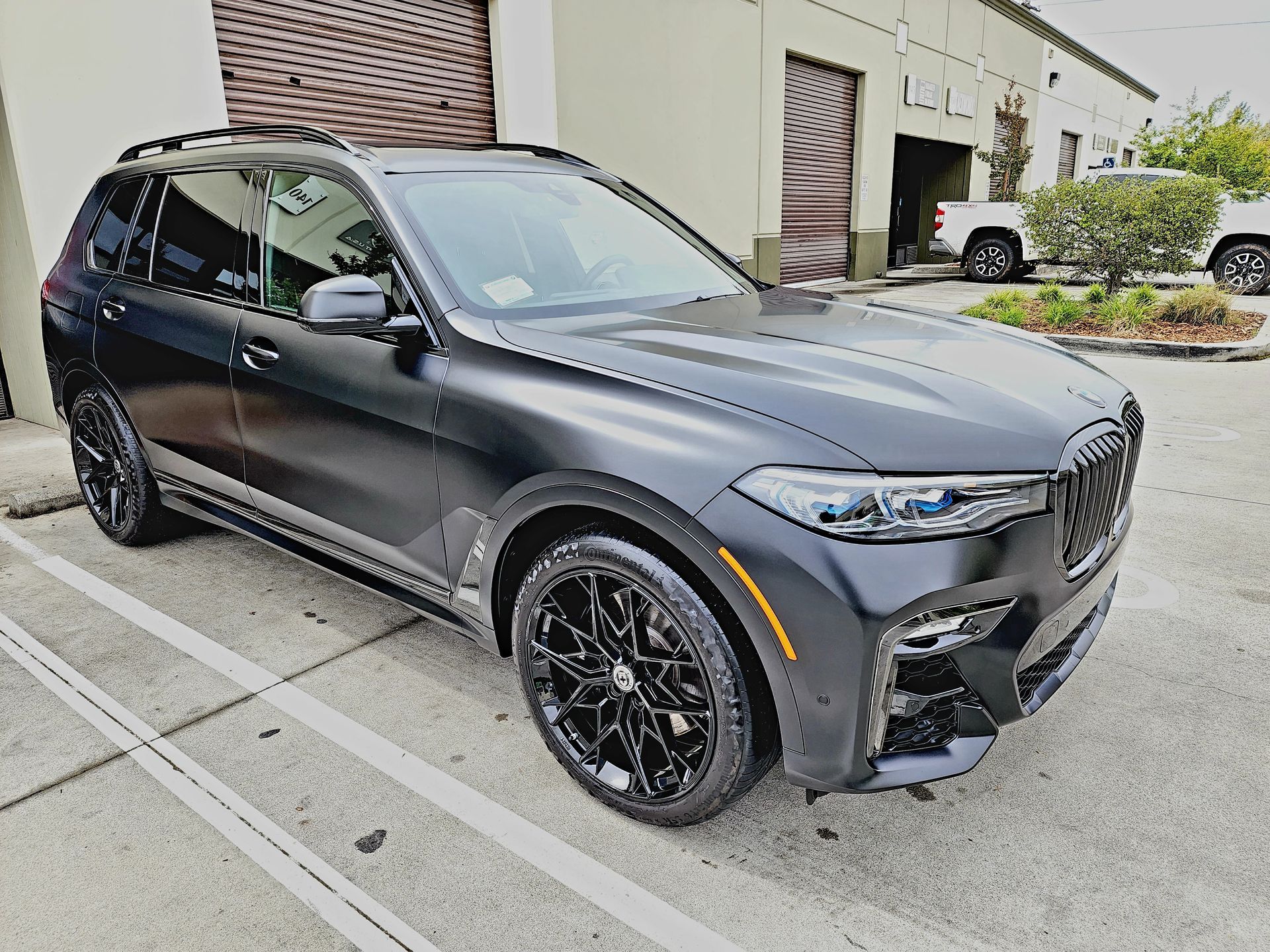 A black bmw x7 is parked in a parking lot in front of a building.
