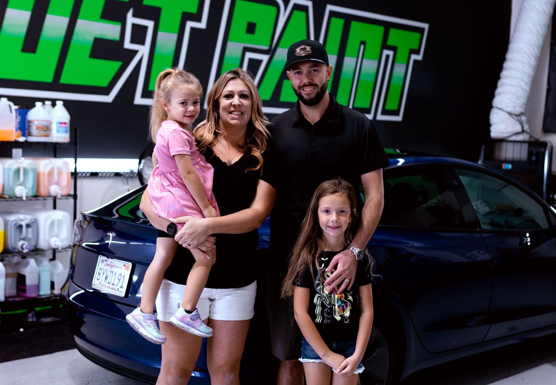 A family is posing for a picture in front of a car.