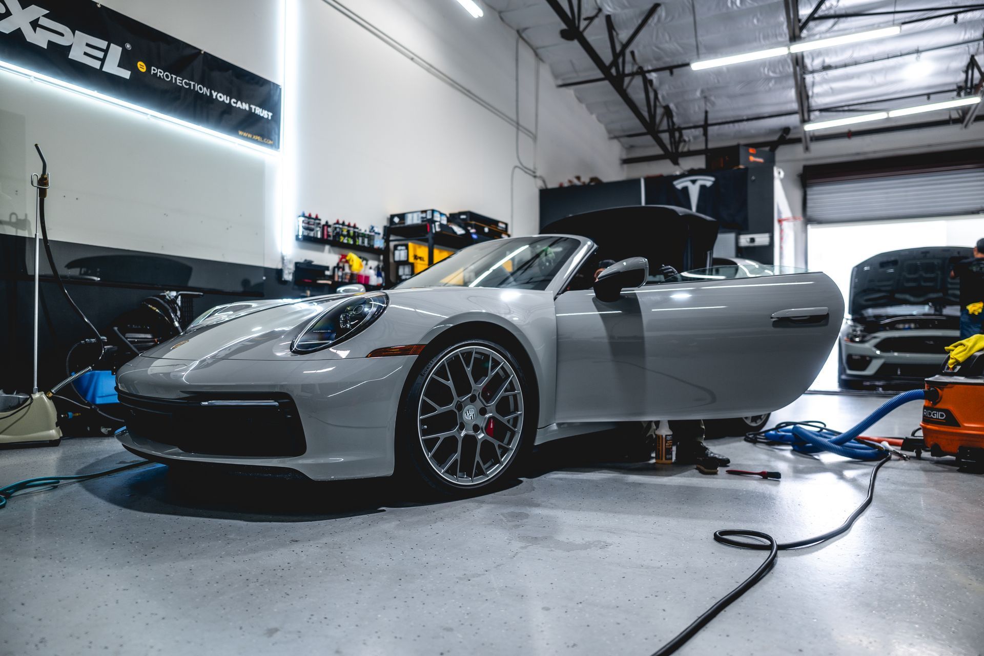 Gray Porsche convertible in a workshop, door open, under repair.