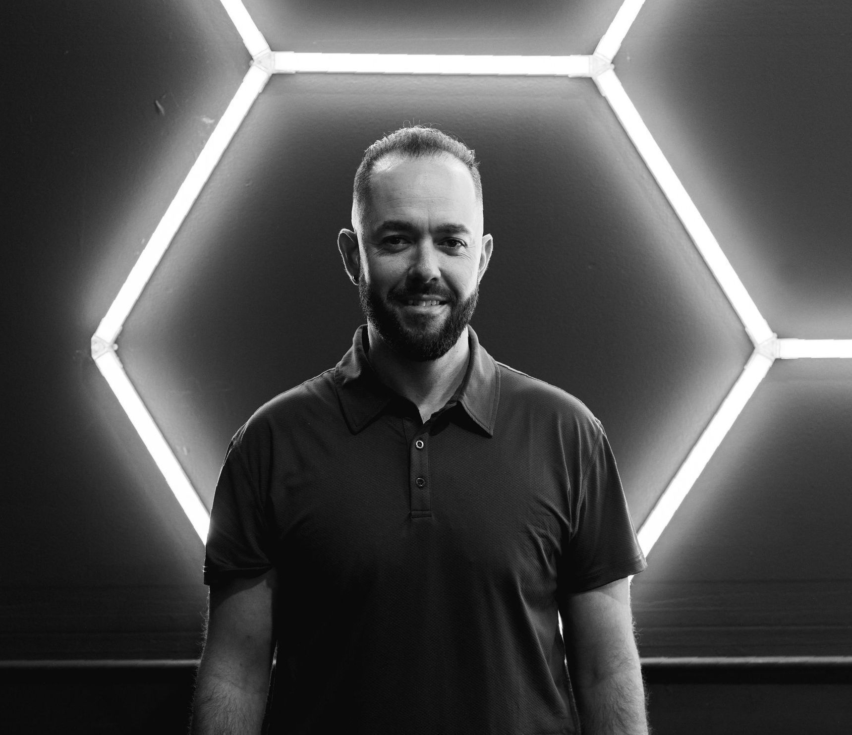 A man with a beard is standing in front of a wall with glowing lights.