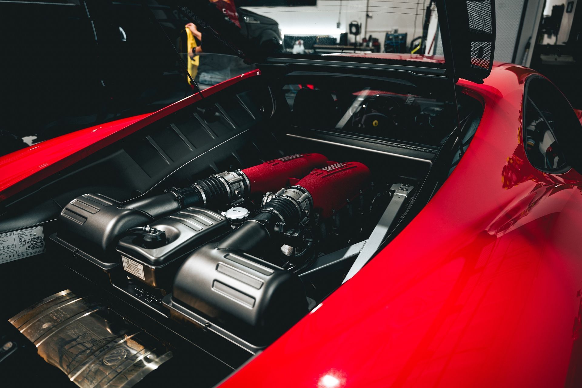 The engine of a red sports car is shown with the hood open.