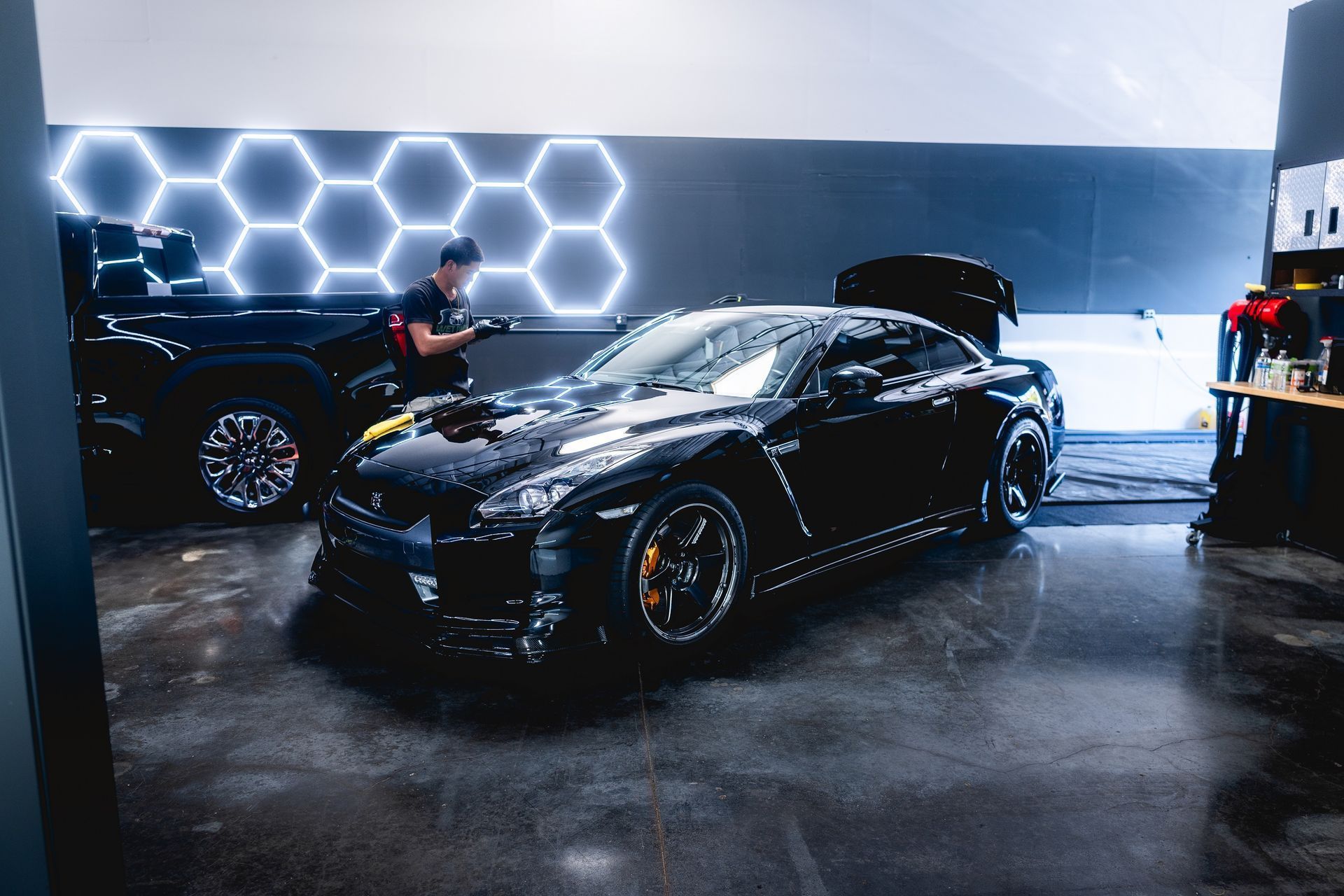 A man is standing next to a black sports car in a garage.