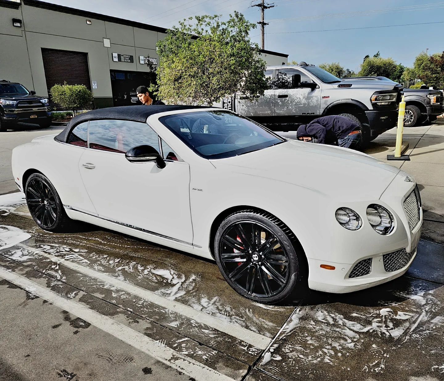 A white bentley convertible is being washed in a parking lot.