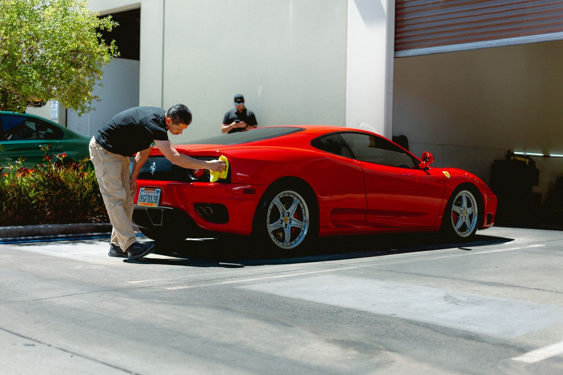 A man is washing a red sports car in a parking lot