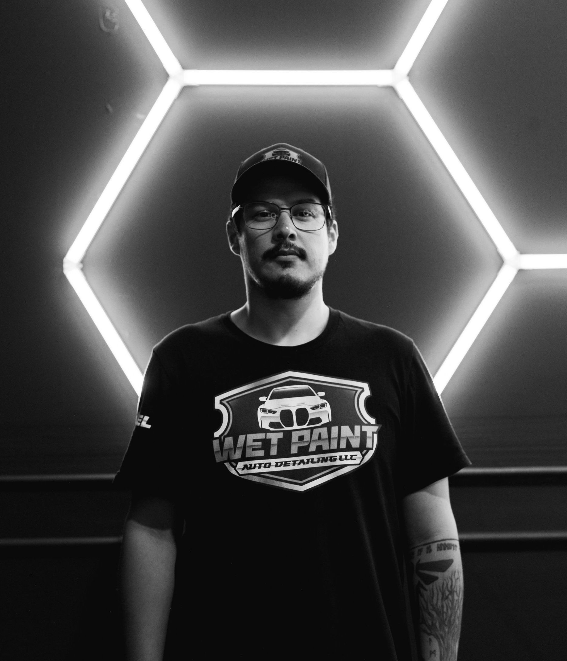 A man wearing a wet paint shirt is standing in front of a neon sign.