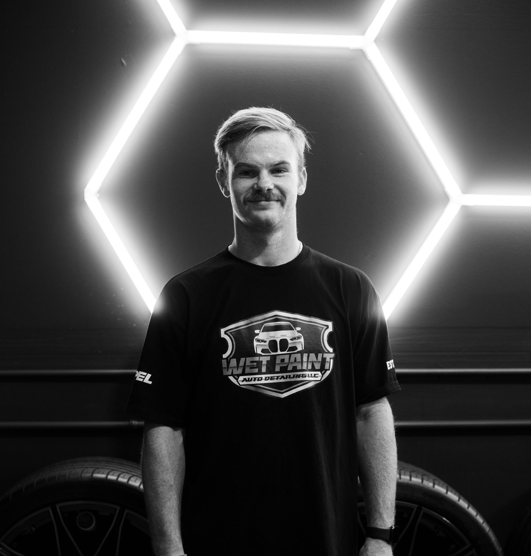 A man is standing in front of a car in a black and white photo.