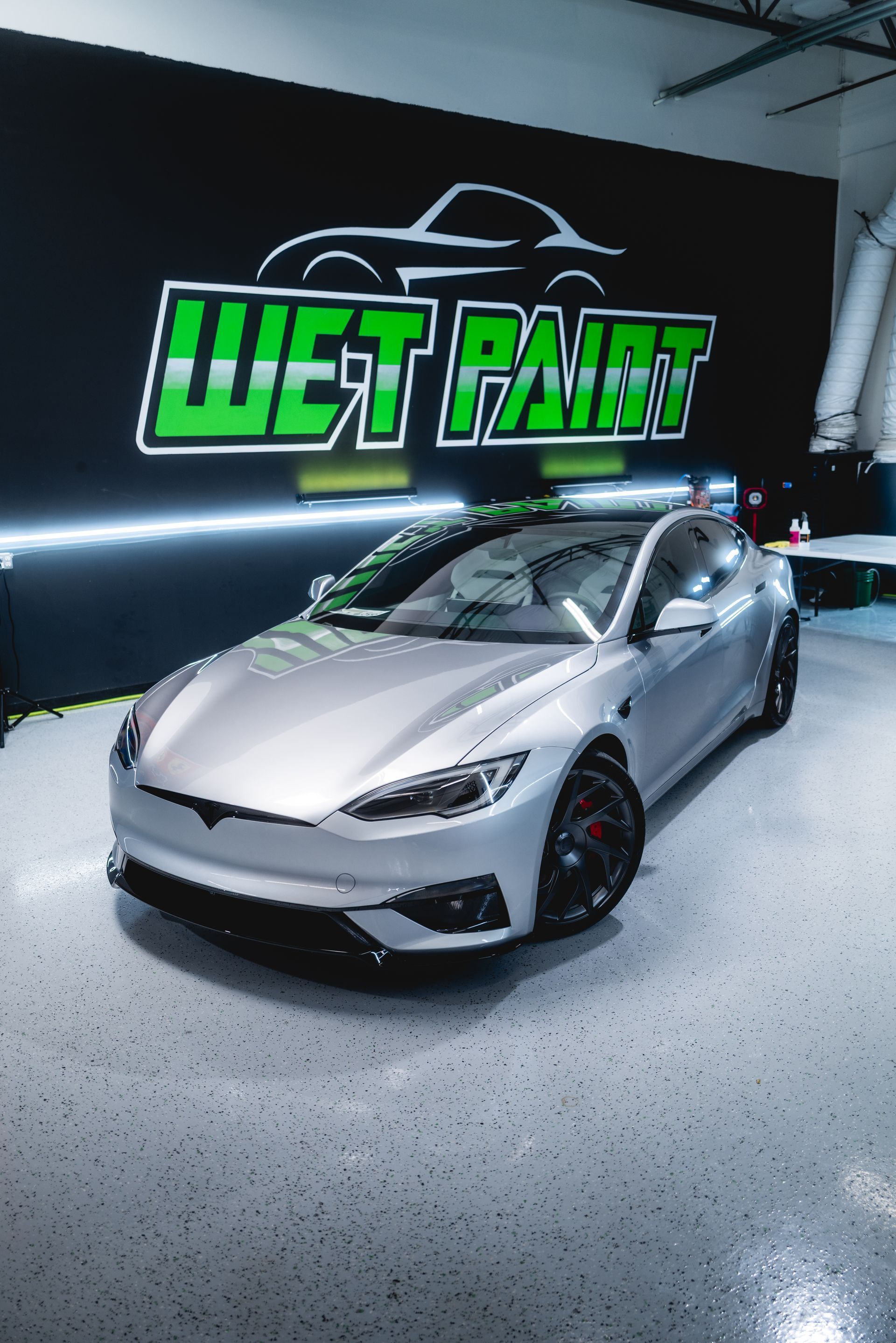 A silver Tesla Model S parked in a workshop with a 