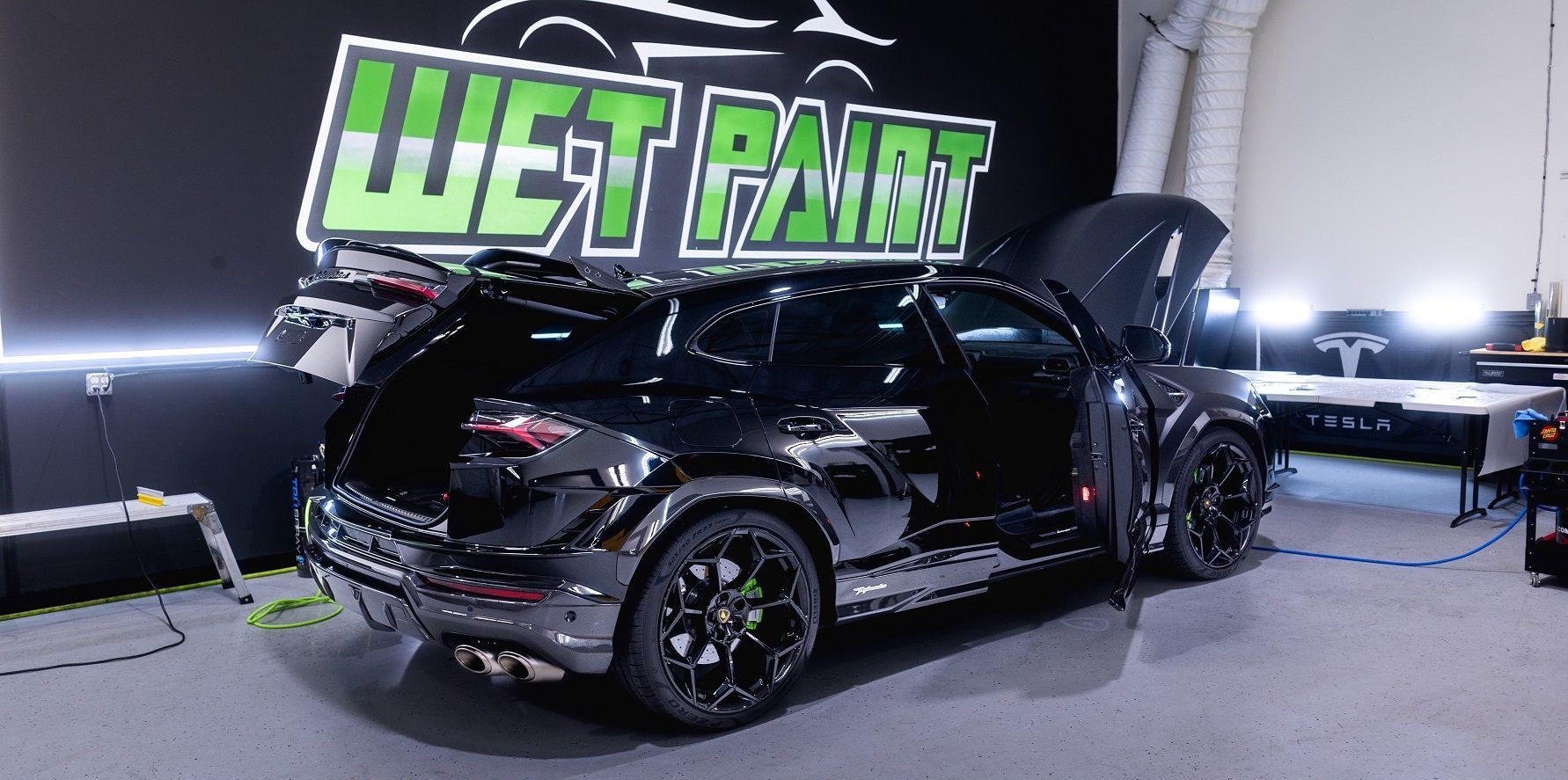 A black car is parked in a garage with the hood open.