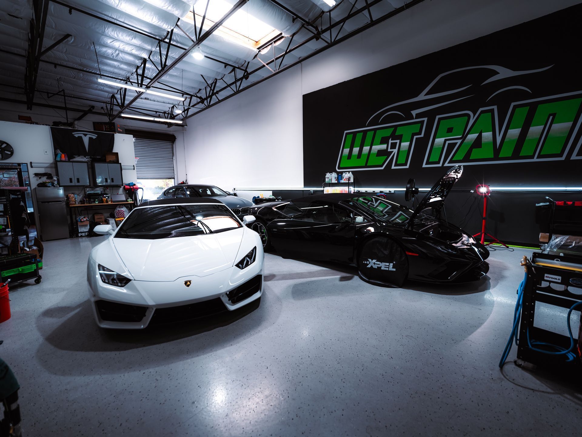 Two sports cars are parked in a garage in front of a wet paint sign.