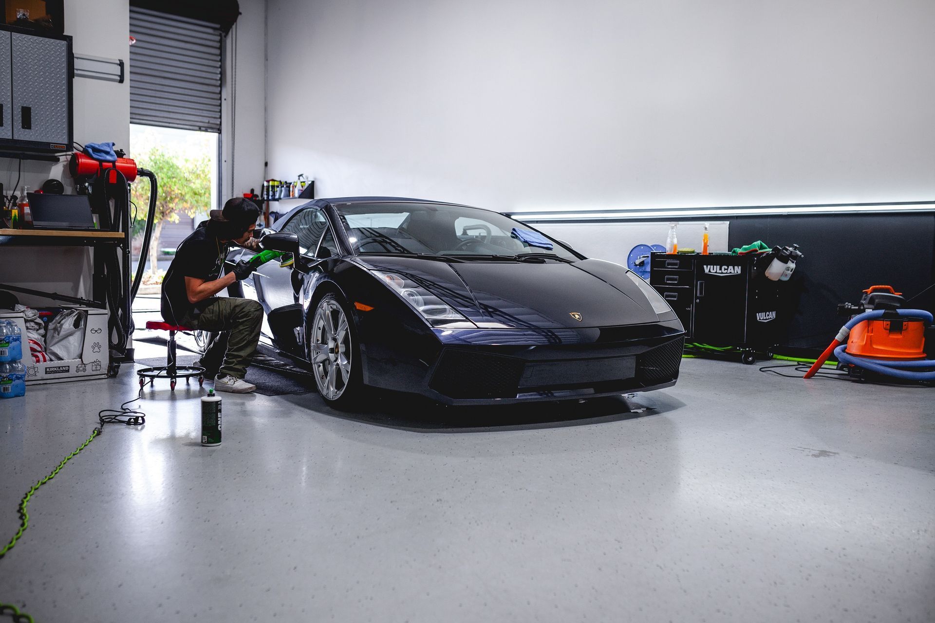A man is polishing a black sports car in a garage.