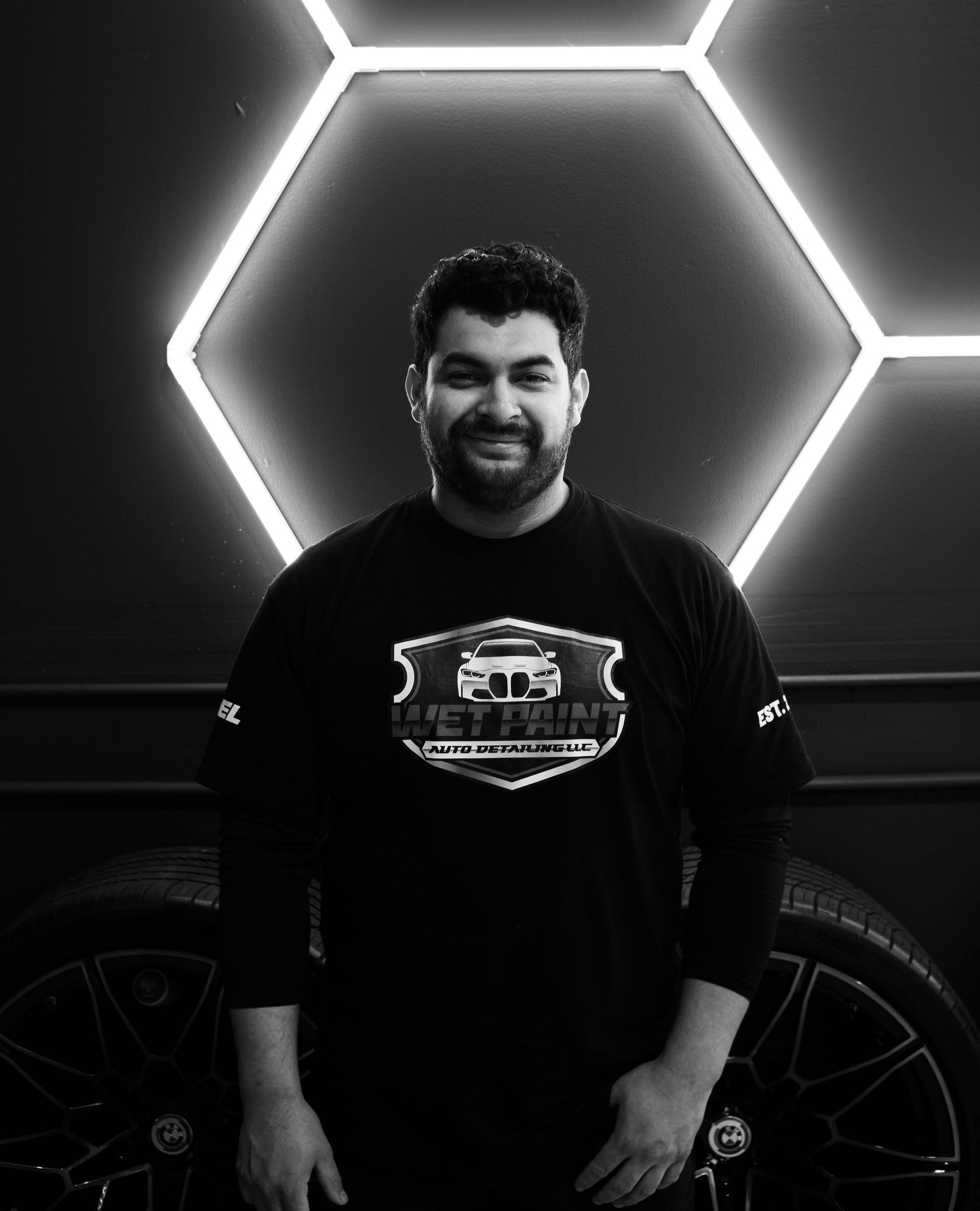 A man with a beard is standing in front of a car in a black and white photo.