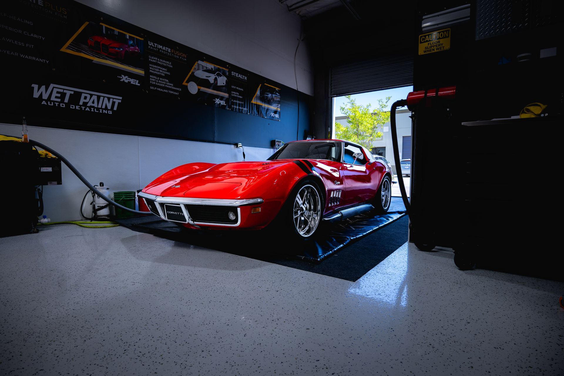 Red classic Corvette in a garage, on a lift, with equipment.