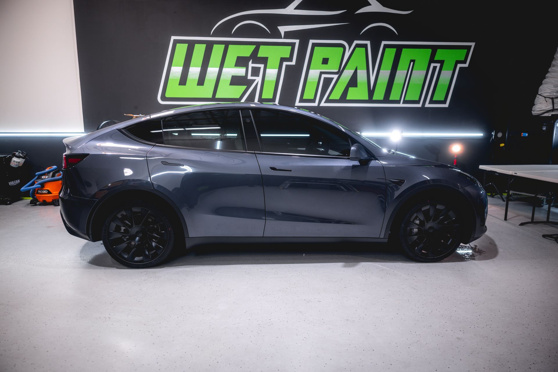 A tesla model y is parked in front of a wet paint sign.