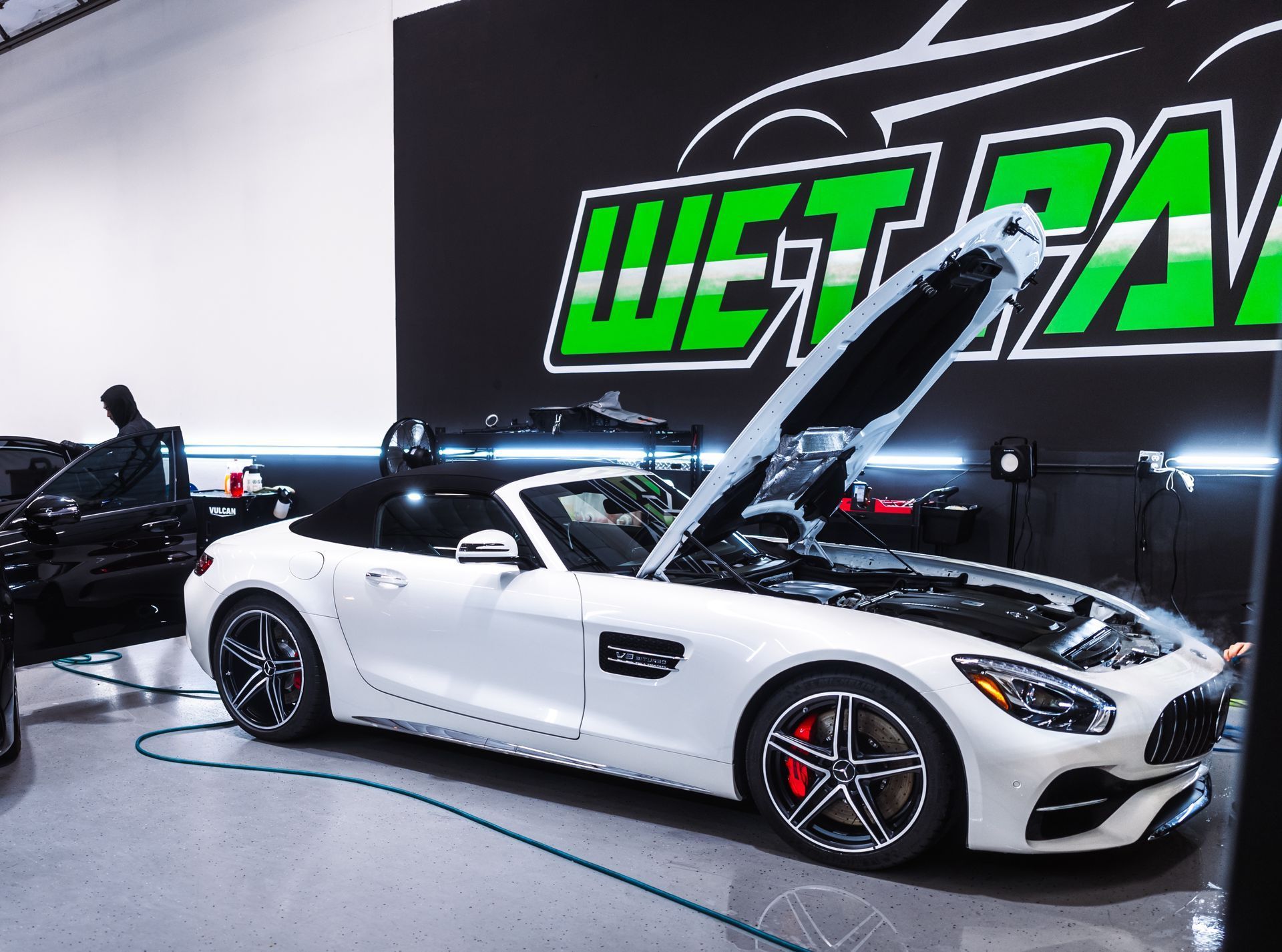 A white sports car is parked in a garage with its hood open.