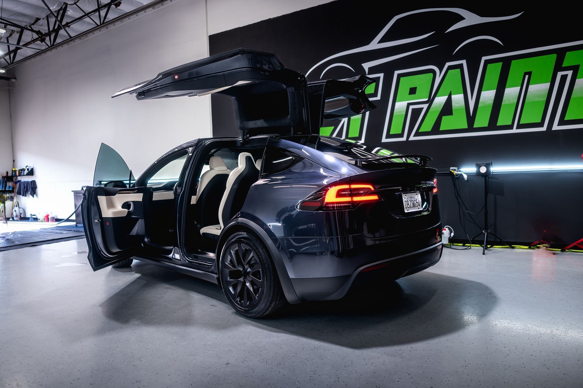 A tesla model x is parked in a garage with its doors open.