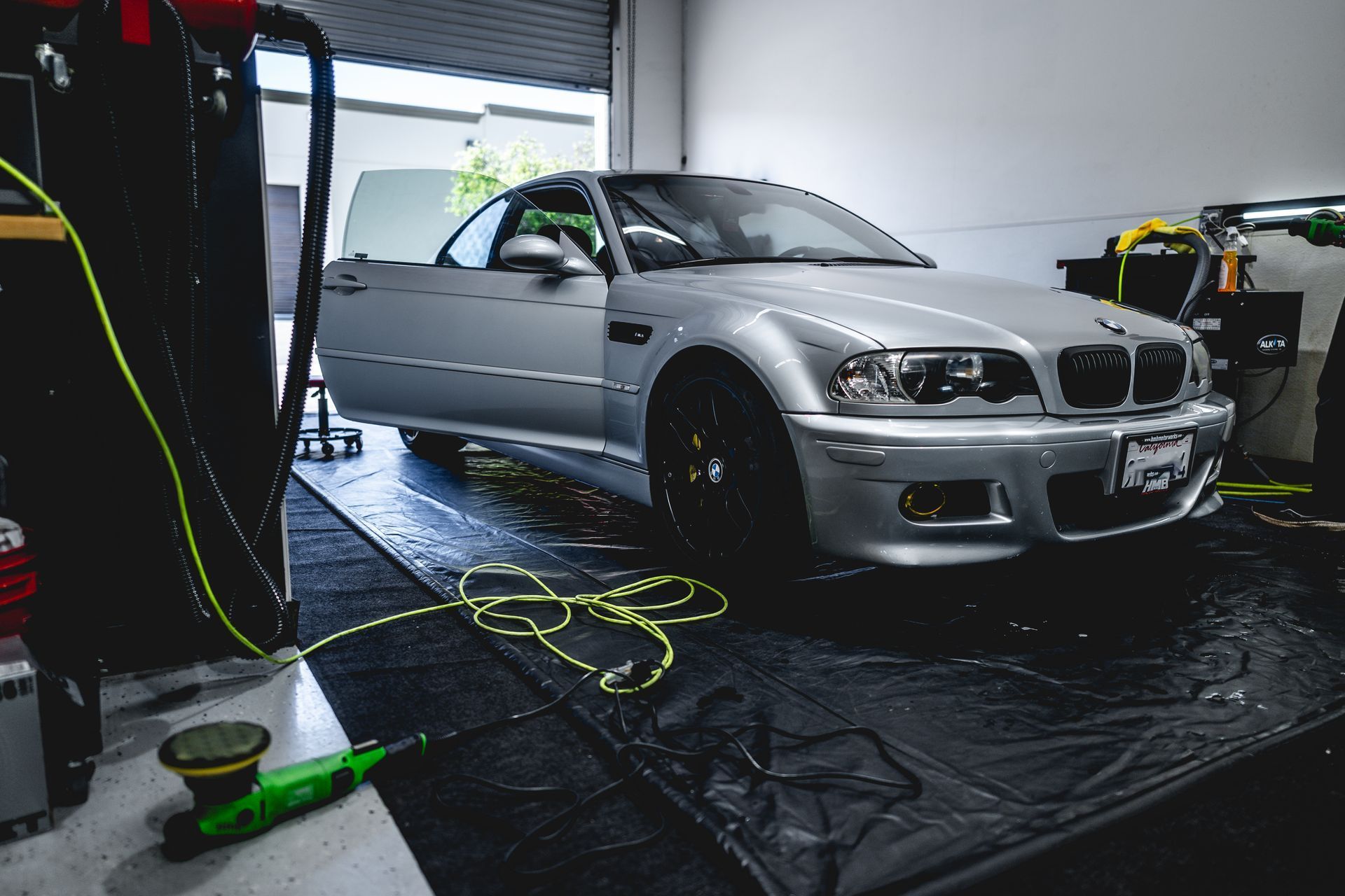 Silver BMW M3 with open door inside a garage, next to tools and equipment.