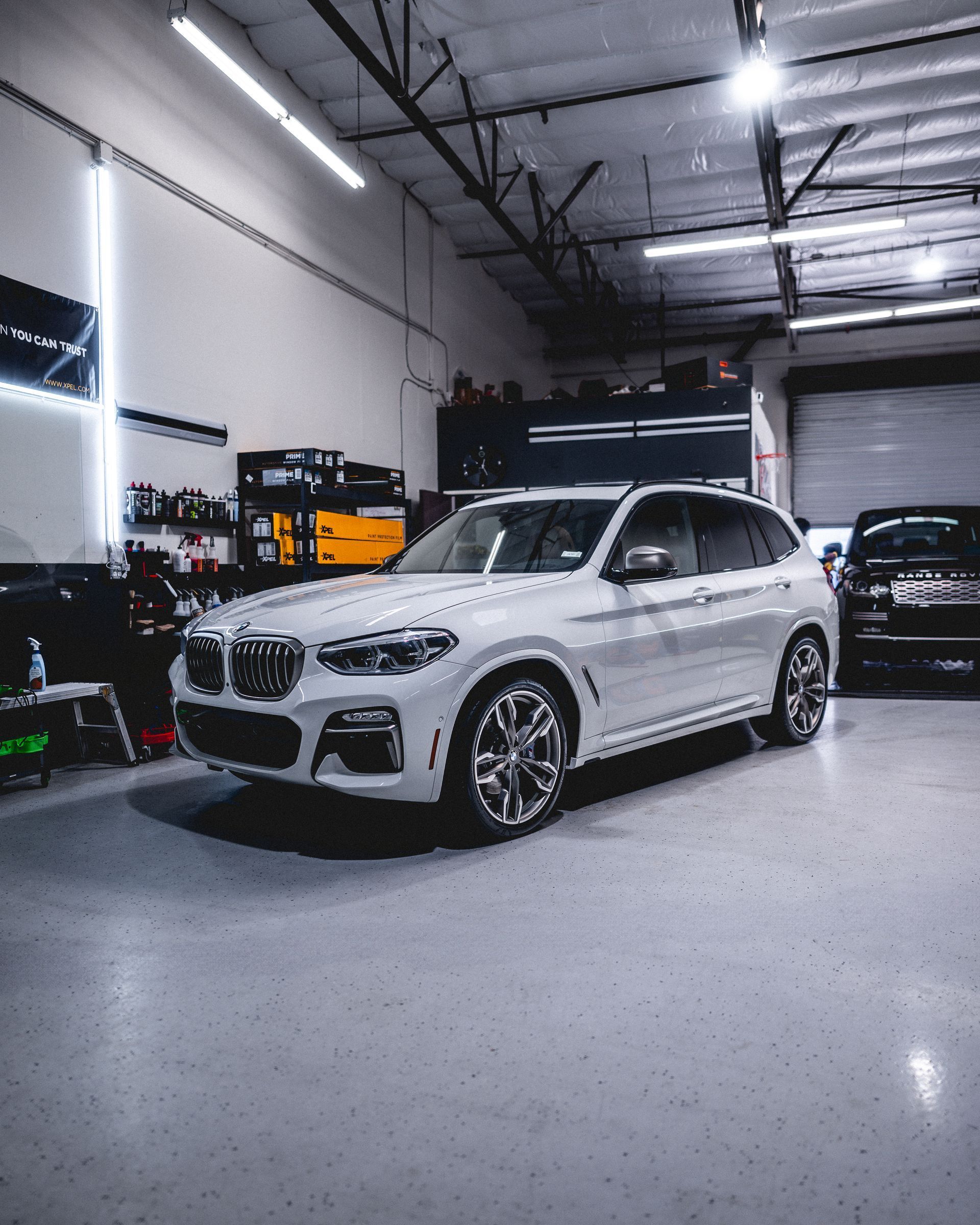 White BMW SUV parked inside a well-lit garage, another dark vehicle visible in the background.