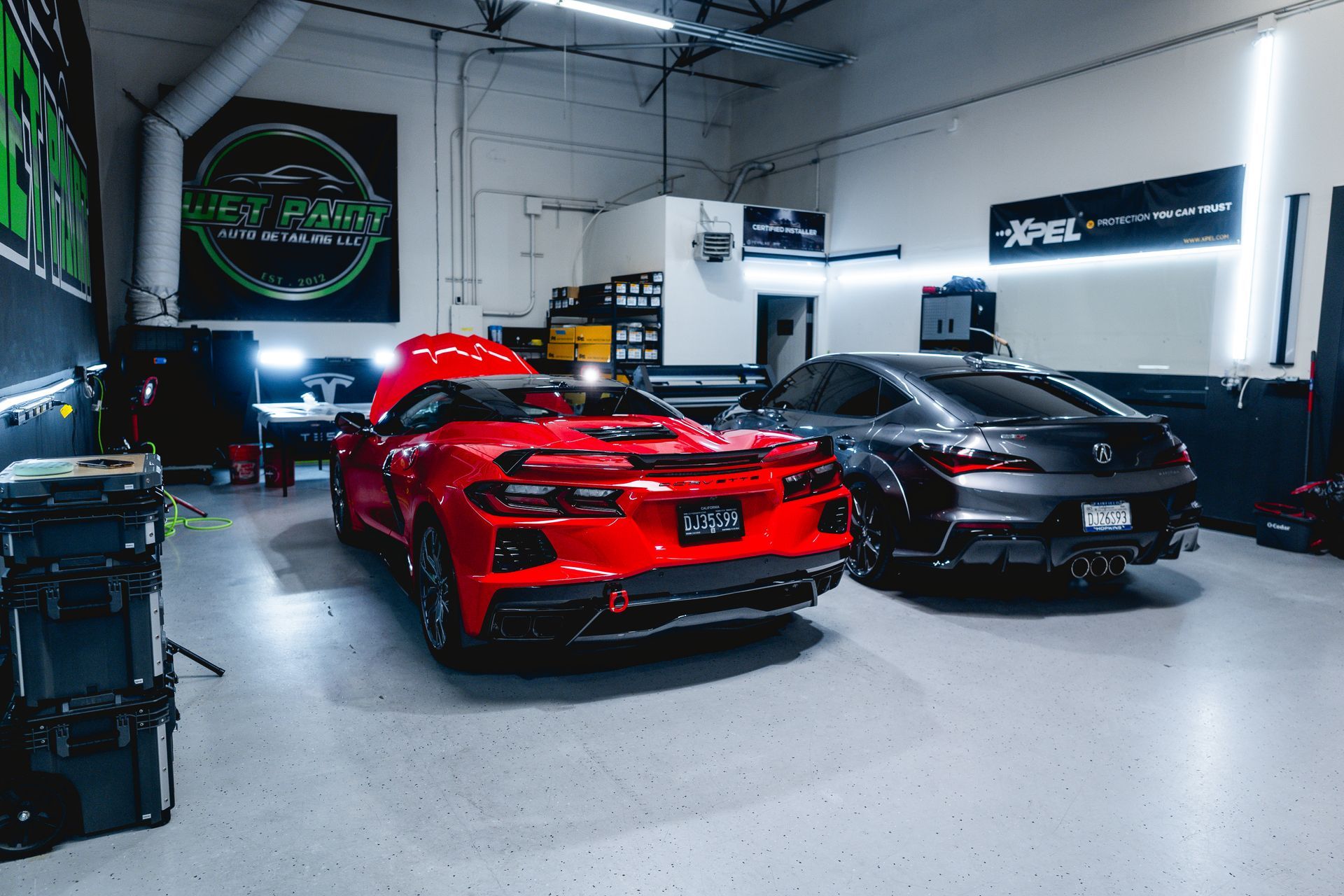 Red sports car and gray sedan in a shop with tools and XPEL signage.